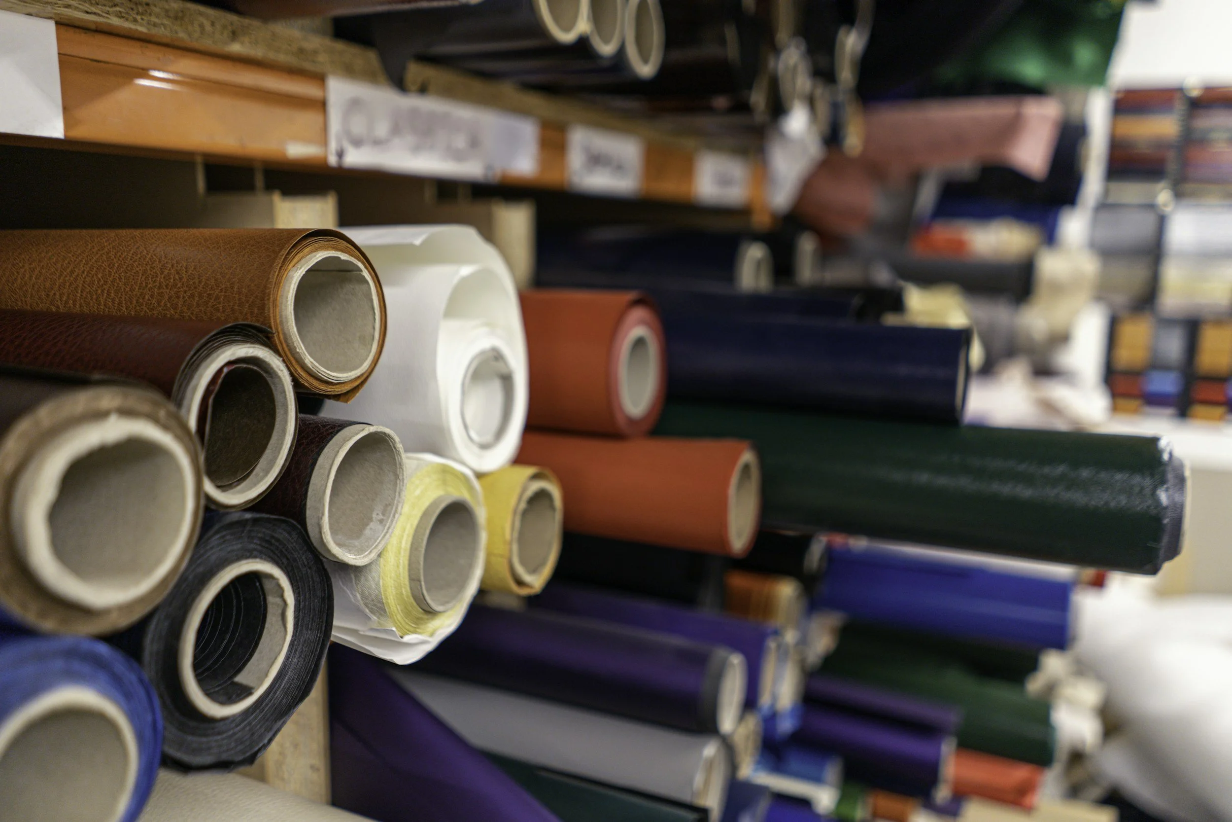 Rotoli di marziale da rilegatura in diversi colori, disposti su scaffali in una legatoria artigianale