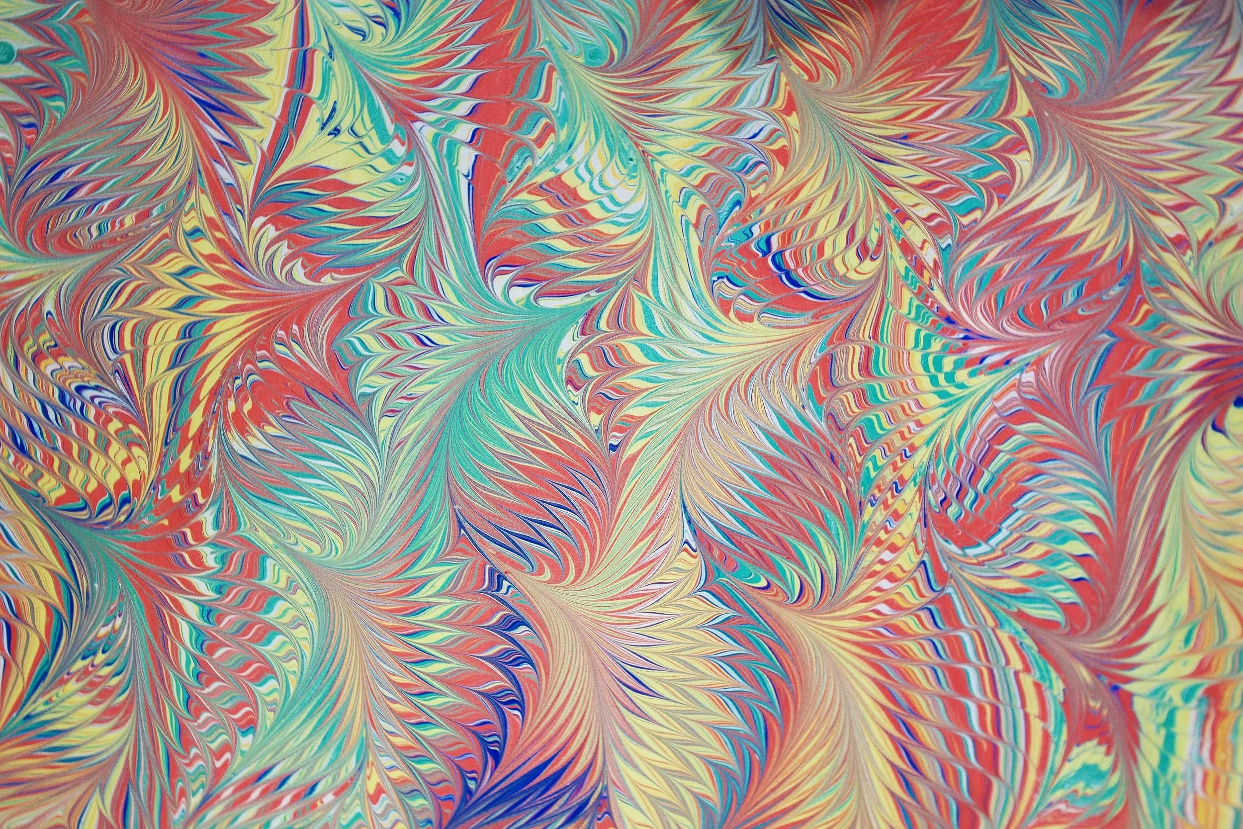 Foto di un foglio di carta fiorentina multicolore, decorato con una marmorizzazione nei toni del rosso, verde acqua, blu e giallo, con venature e sfumature che si intrecciano sulla superficie.