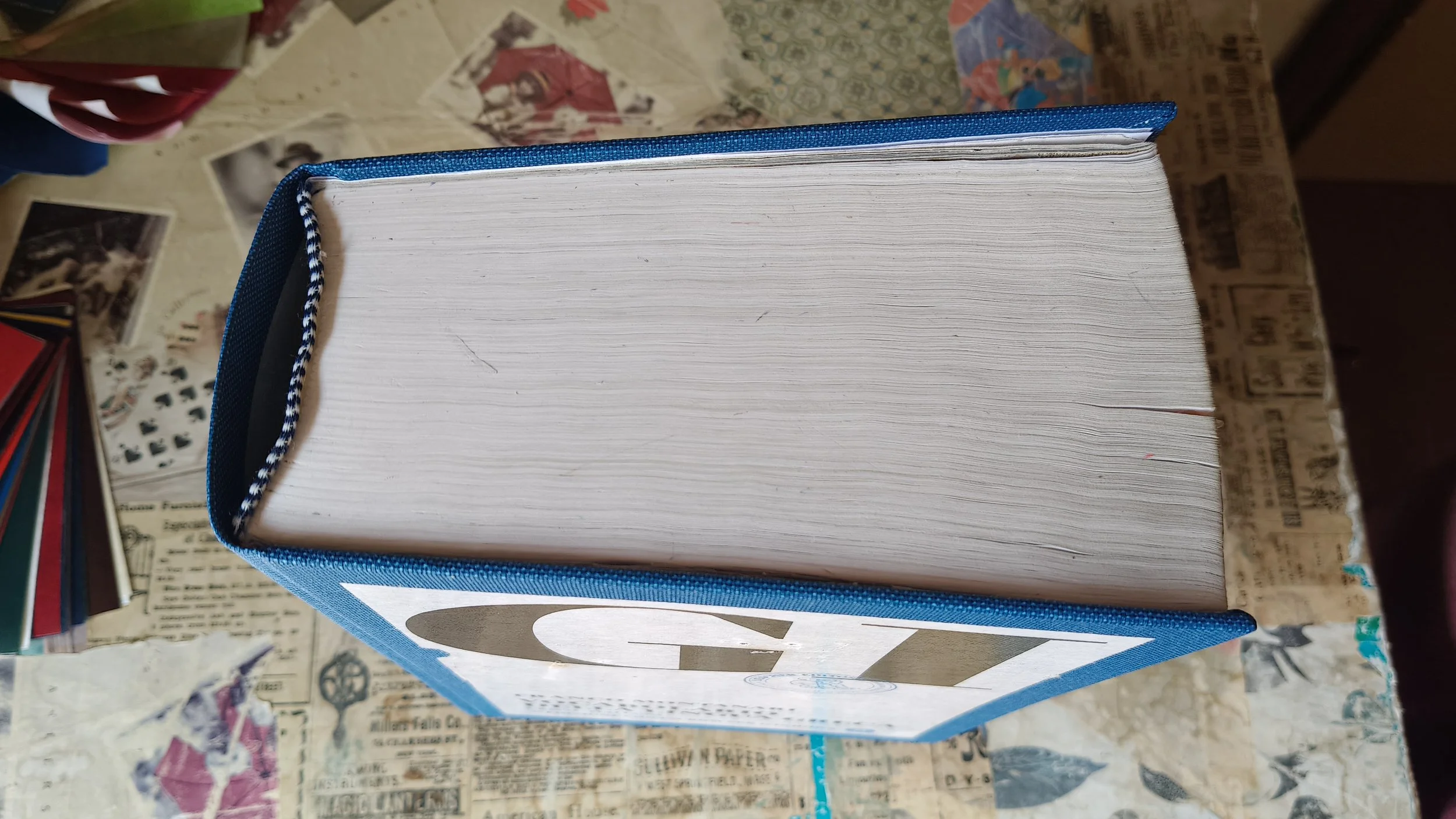 Vista dall'alto del Vocabolario della lingua greca di Franco Montanari, restaurato con copertina in buckram blu, toppa della copertina originale applicata e capitello bicolore blu e bianco.