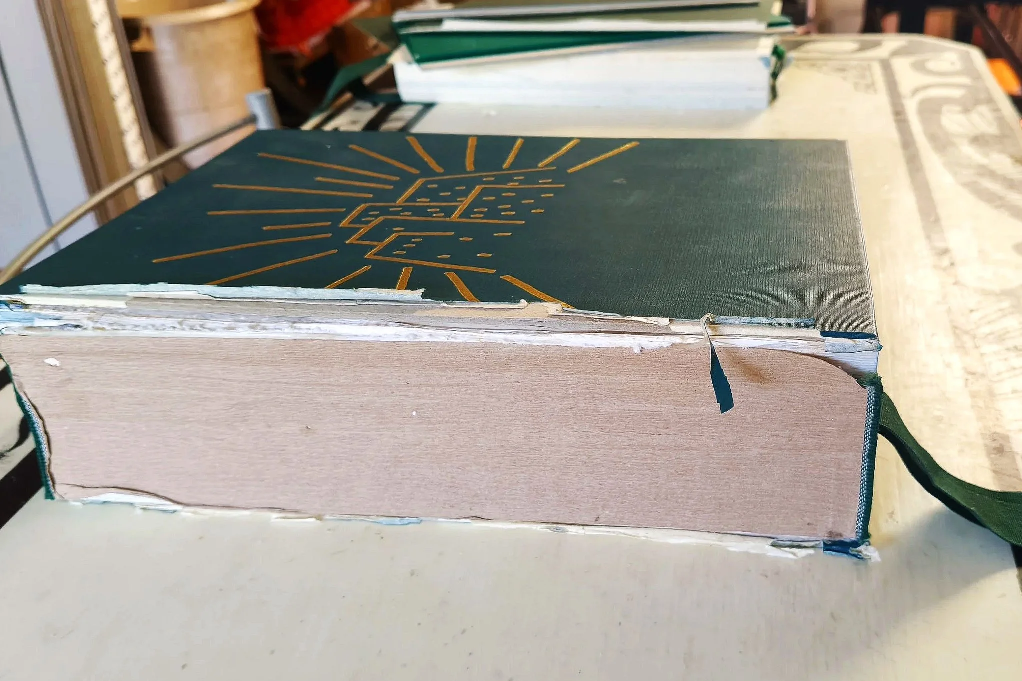 Foto di un lezionario con copertina in ecopelle verde, decorata da un motivo dorato al centro, e dorso staccato prima del restauro.