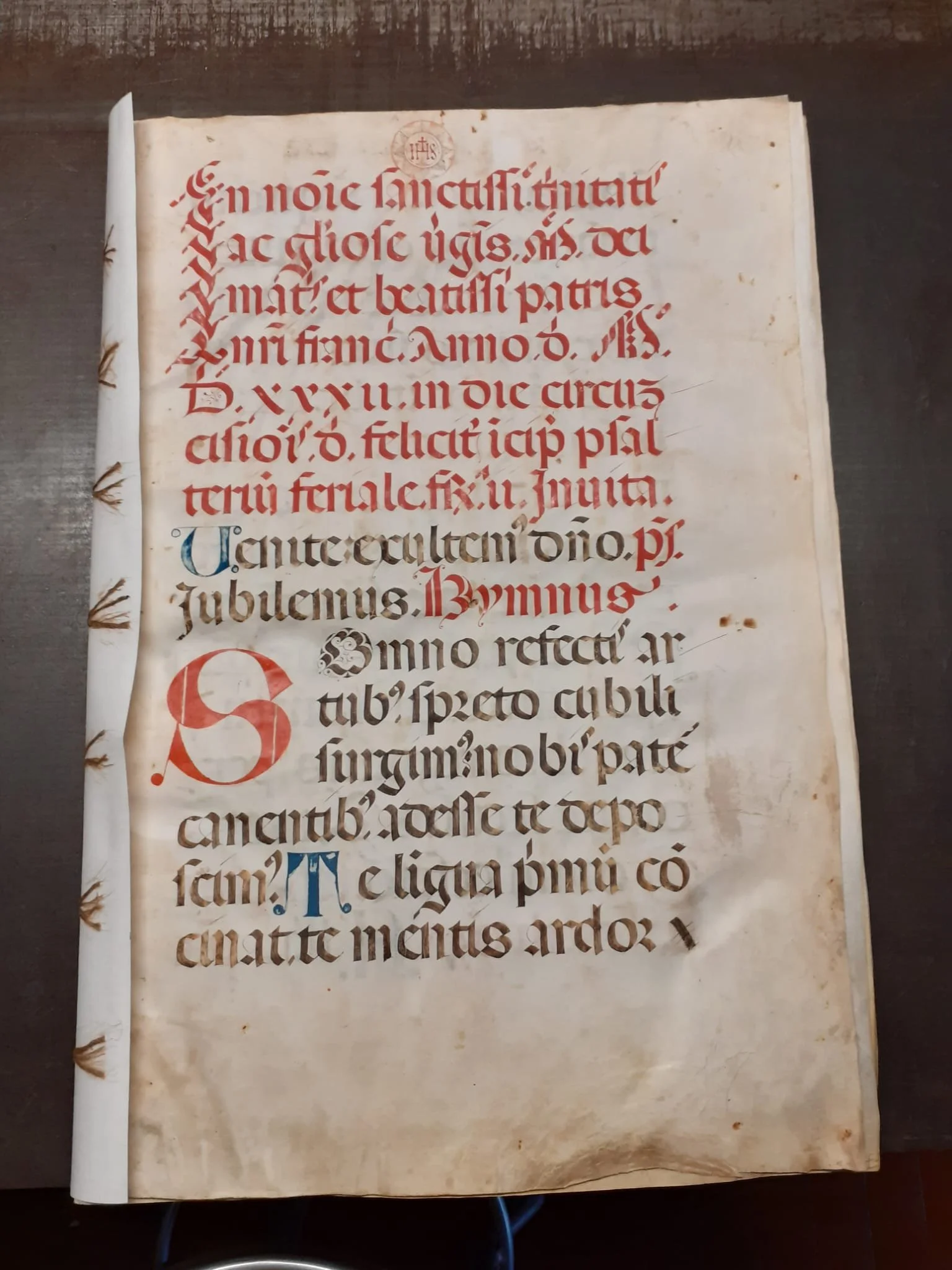 Pagina di un manoscritto del 1400 medievale con testo in lettere gotiche, alcune parti in rosso e altre in nero, decorazioni e iniziali elaborate, dopo il restauro.