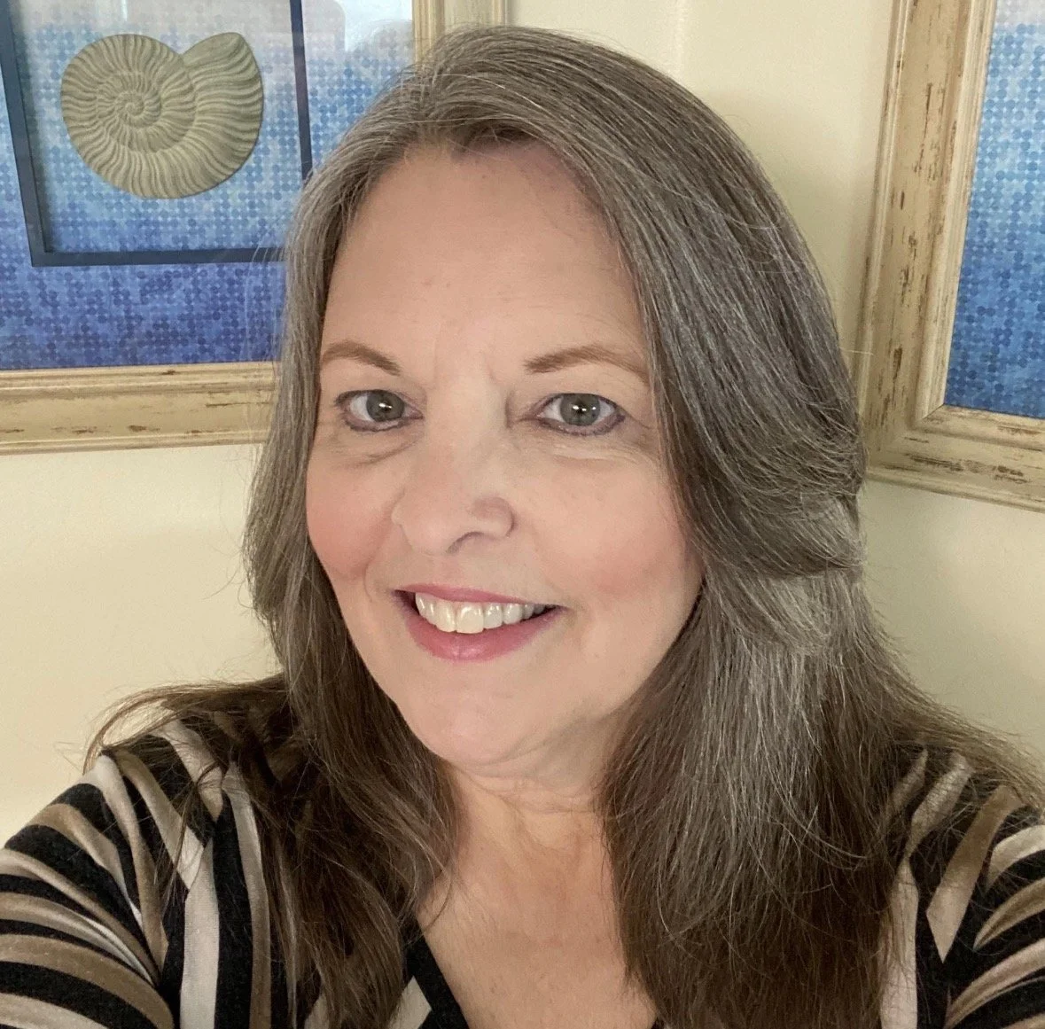 A woman smiling for a selfie in front of framed artwork featuring a spiral seashell and blue textured background.