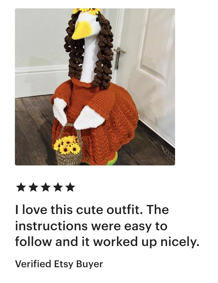A handmade knitted costume of a woman with a white face and yellow beak, dressed as a stork or heron, with brown curly yarn hair, an orange dress, and a sunflower headband. The costume includes a small basket with yellow flowers.