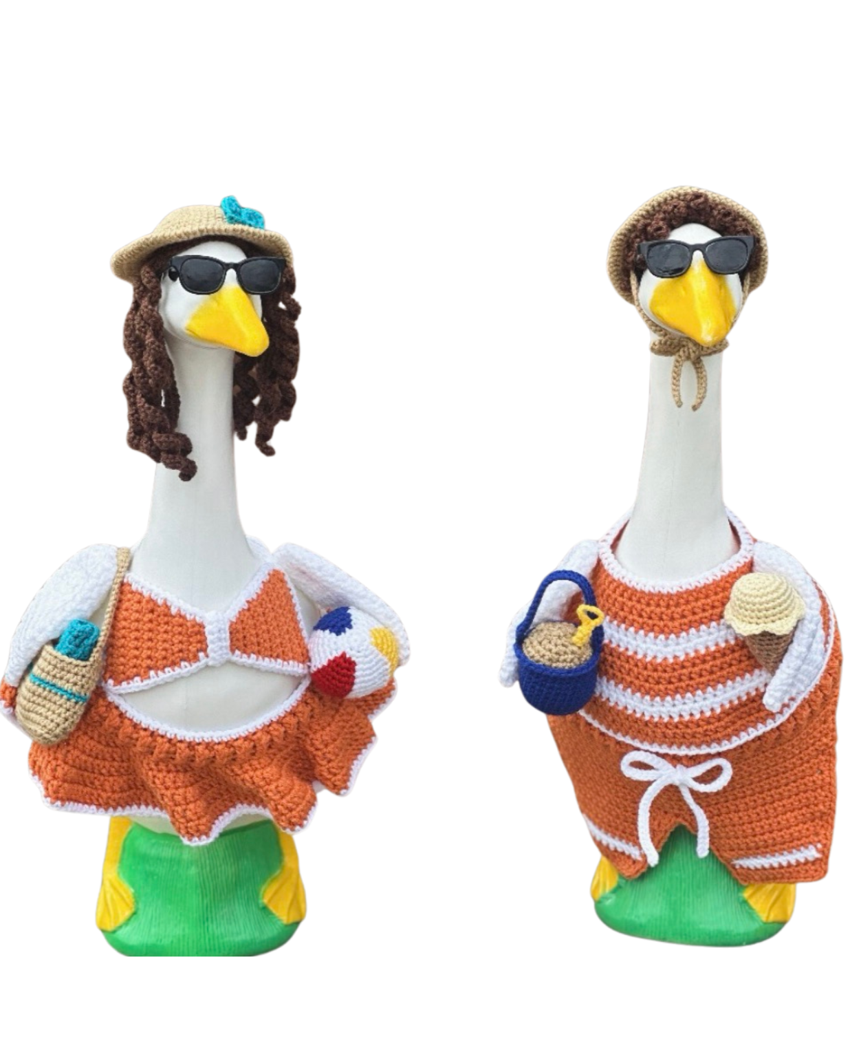 Two cartoon-style stork figurines dressed in beachwear and sunglasses, with knitted hats, carrying beach accessories like a bottle, volleyball, ice cream, and pail.