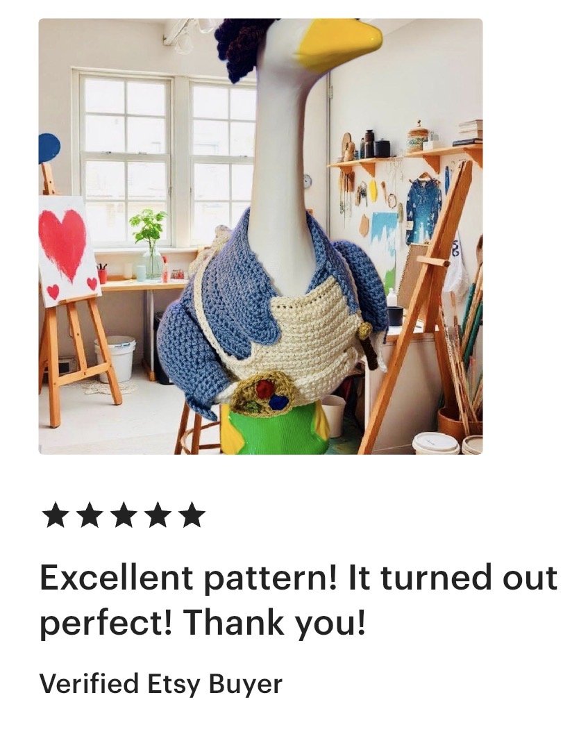 A large sculpture of a swan with a yellow beak and black hair, dressed in a blue and cream knitted sweater in an art studio.