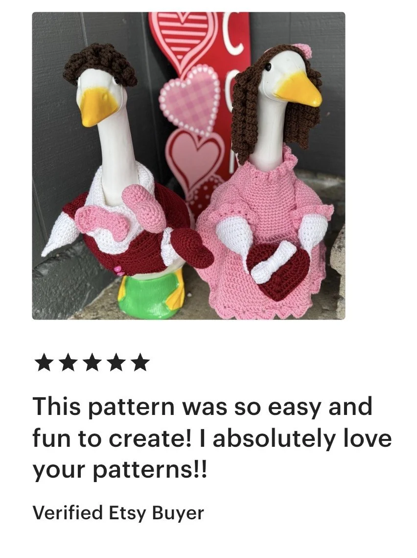 Two goose figurines dressed in pink and red crocheted outfits holding hearts, with a Valentine's Day themed background.