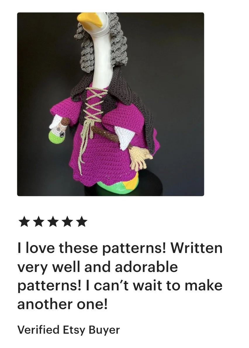 A crocheted stuffed animal resembling a goose dressed as a medieval knight, with a pink dress, brown cape, and gray curly hair, standing against a black background.