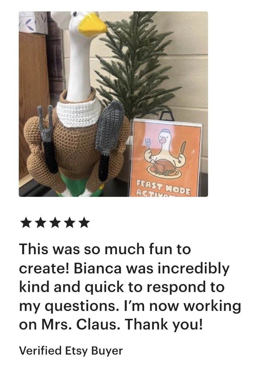 Decorative plush turkey with a long neck, white crocheted neck wrap, and crocheted accessories including a fork, knife, and spatula, positioned next to a small pine tree and a sign that reads 'Feast Mode Activated' with an illustration of a turkey wi