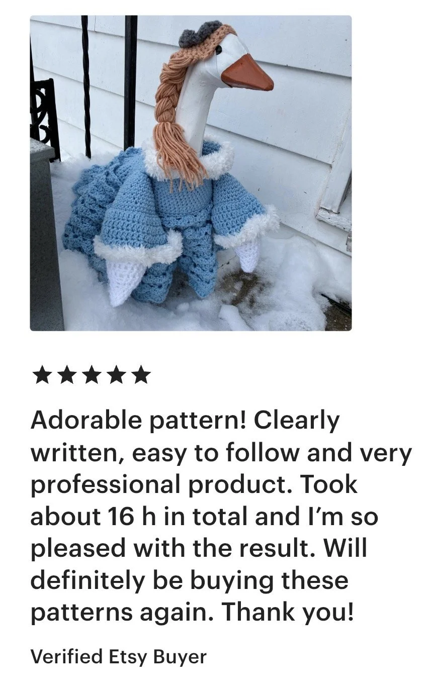 A decorative turkey figure with a wooden head, painted orange beak, and yarn hair, dressed in a blue crocheted outfit with white trim, standing on snow outside a house with white siding.