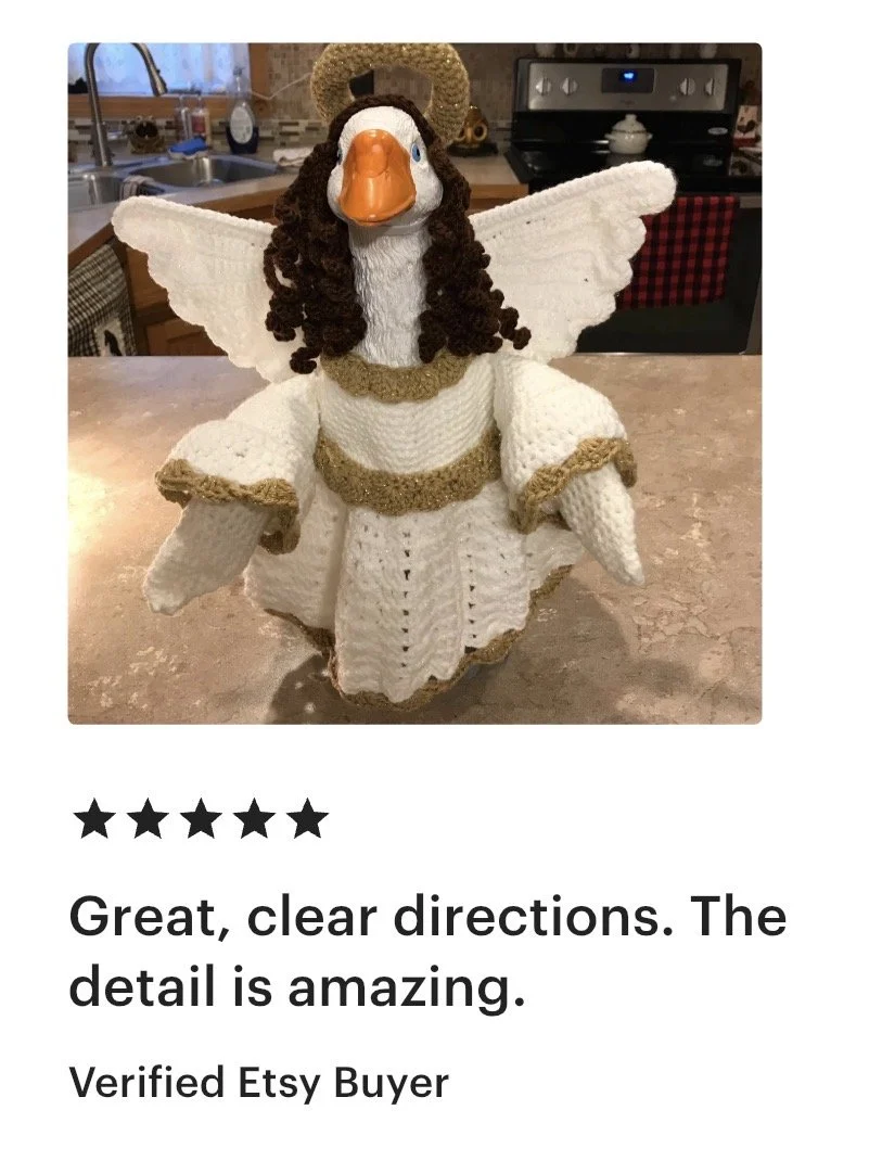 A crocheted angel doll with white wings, a white gown with gold trim, a halo, and a face resembling a duck, placed on a kitchen countertop.