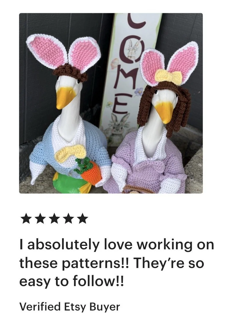 Two decorative duck sculptures dressed as rabbits with knitted clothes and bunny ears, one holding a carrot, set outdoors.