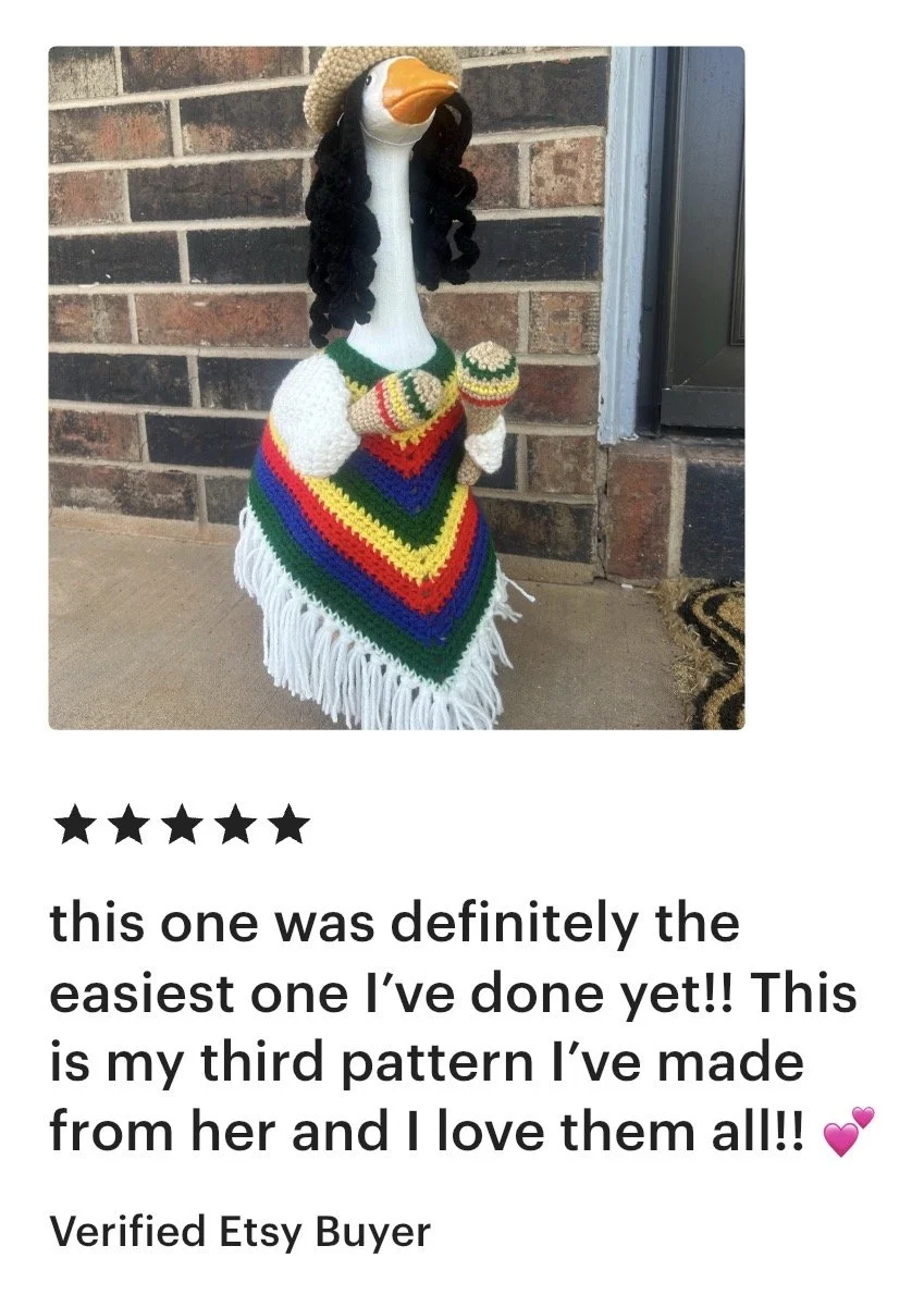 A decorative goose sculpture dressed in a colorful crocheted poncho, knit mittens, and a hat, standing outside against a brick wall.