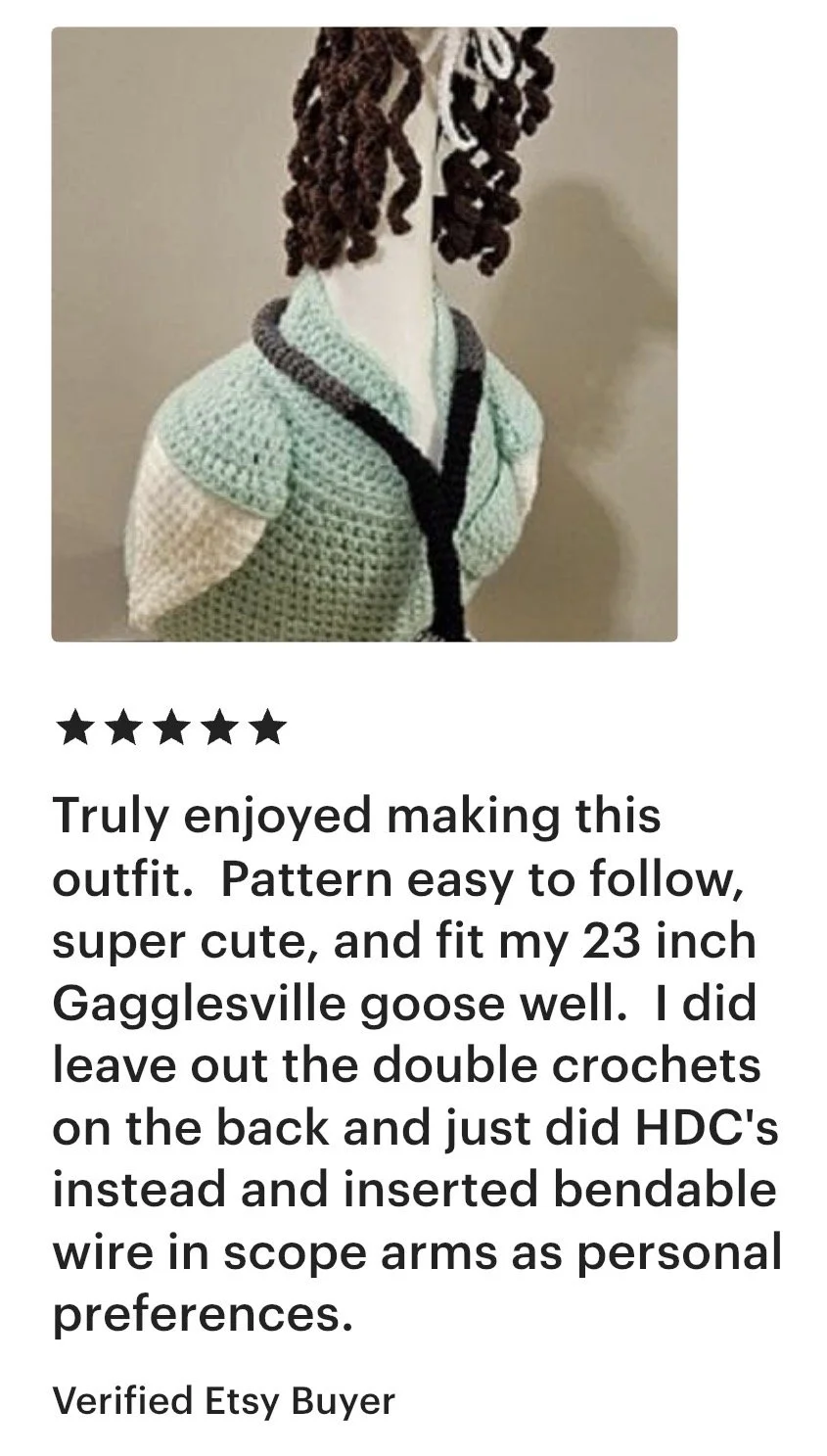 A handmade crochet outfit on a mannequin, featuring a light green top with white and dark gray accents, and a black trim around the collar.