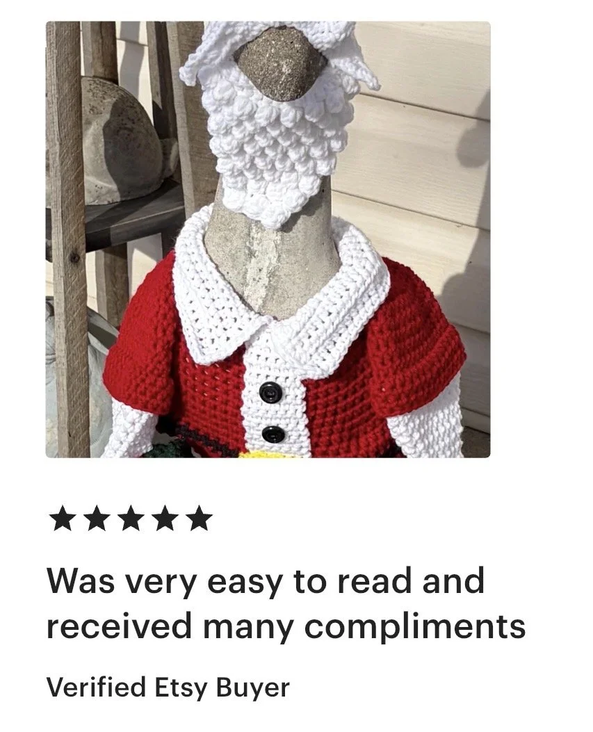 A crocheted Santa Claus figure dressed in a red and white outfit with black buttons, and a white collar, with a white beard and hat, displayed on a mannequin bust.