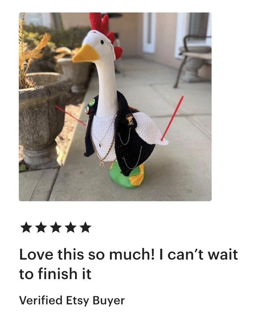 A plush toy resembling a seagull dressed in a black jacket, white sweater, and green shoes, with accessories like pins and chains, standing outdoors on a concrete surface near garden pots.