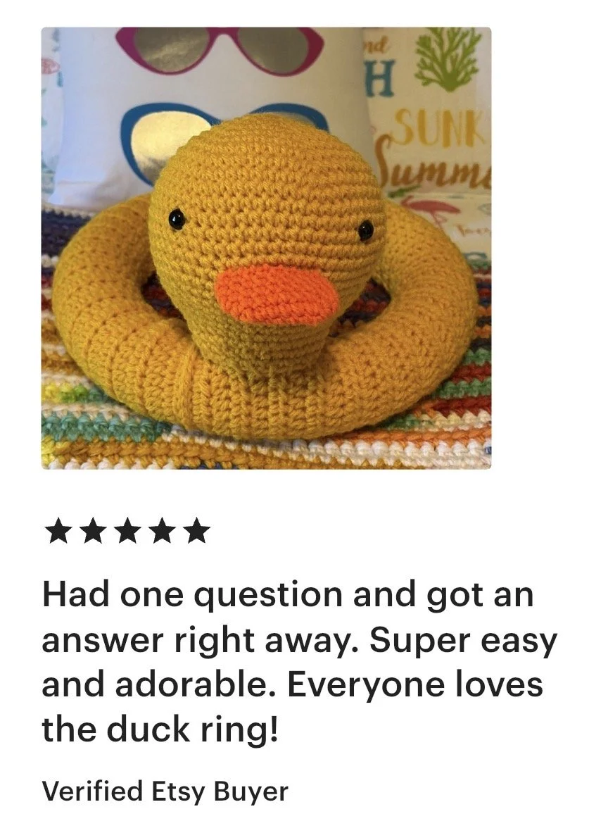 A crocheted yellow duck with an orange beak, black eyes, and a looped body, placed on a colorful knitted surface.