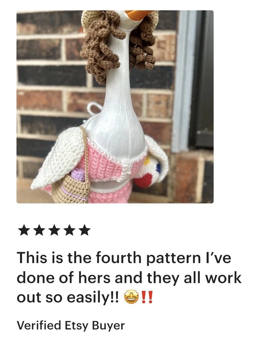 Decorative object resembling a stylized cartoon giraffe with a long neck, crocheted clothing, and yarn hair, standing against a brick wall.