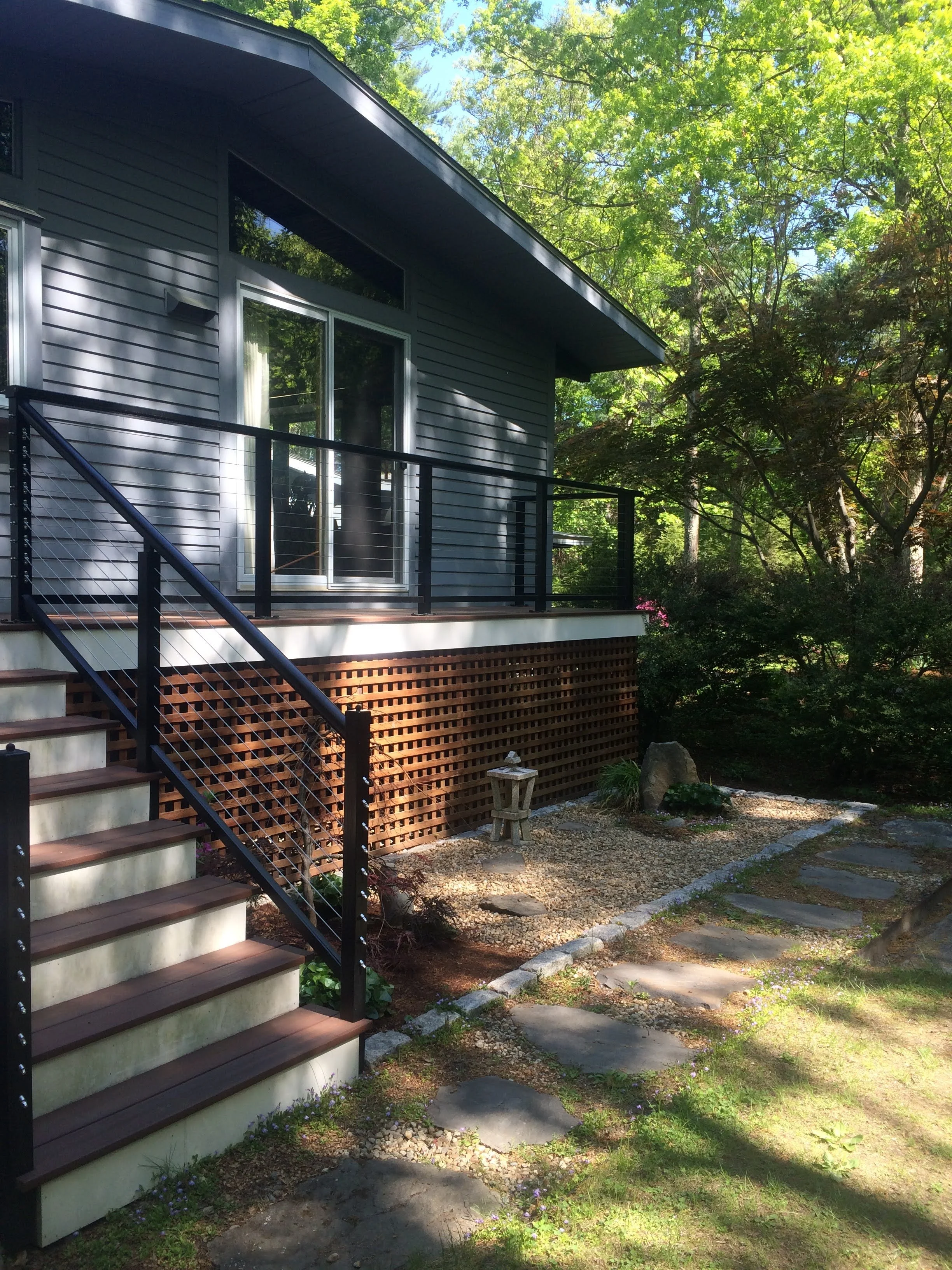 A grey house with a newly added deck based in Stow, MA. Includes new deckboards, railings, posts and string. Beautiful new deck in the woods.
