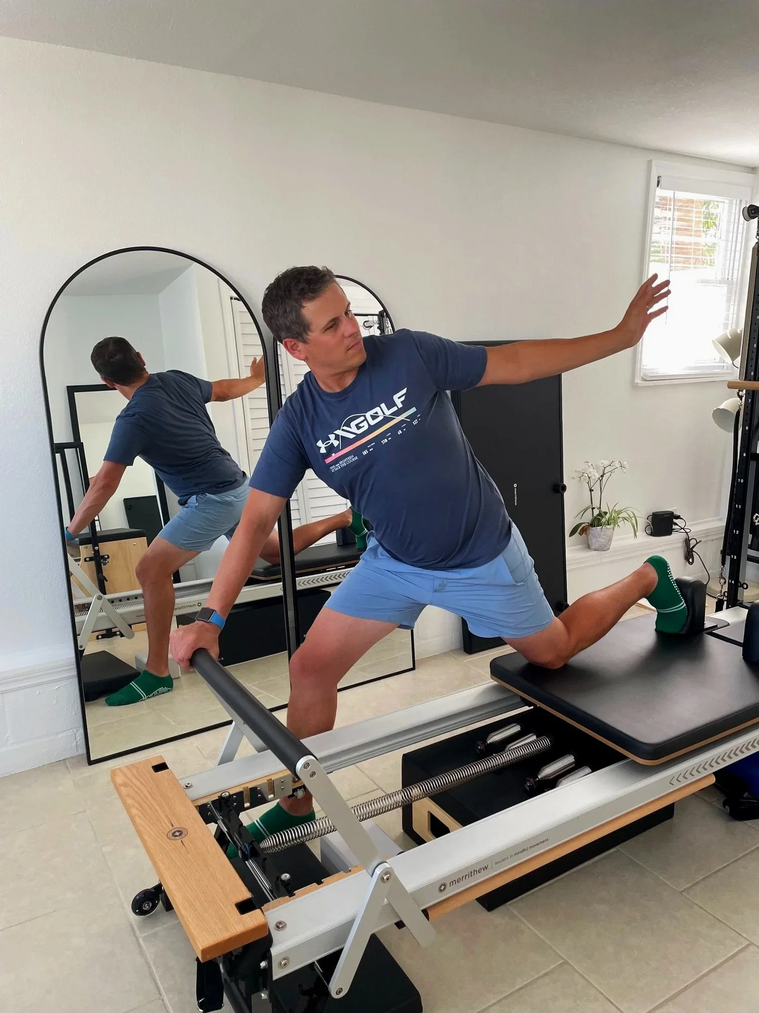 Man doing pilates on fitness equipment, including a reformer machine and a mirror.
