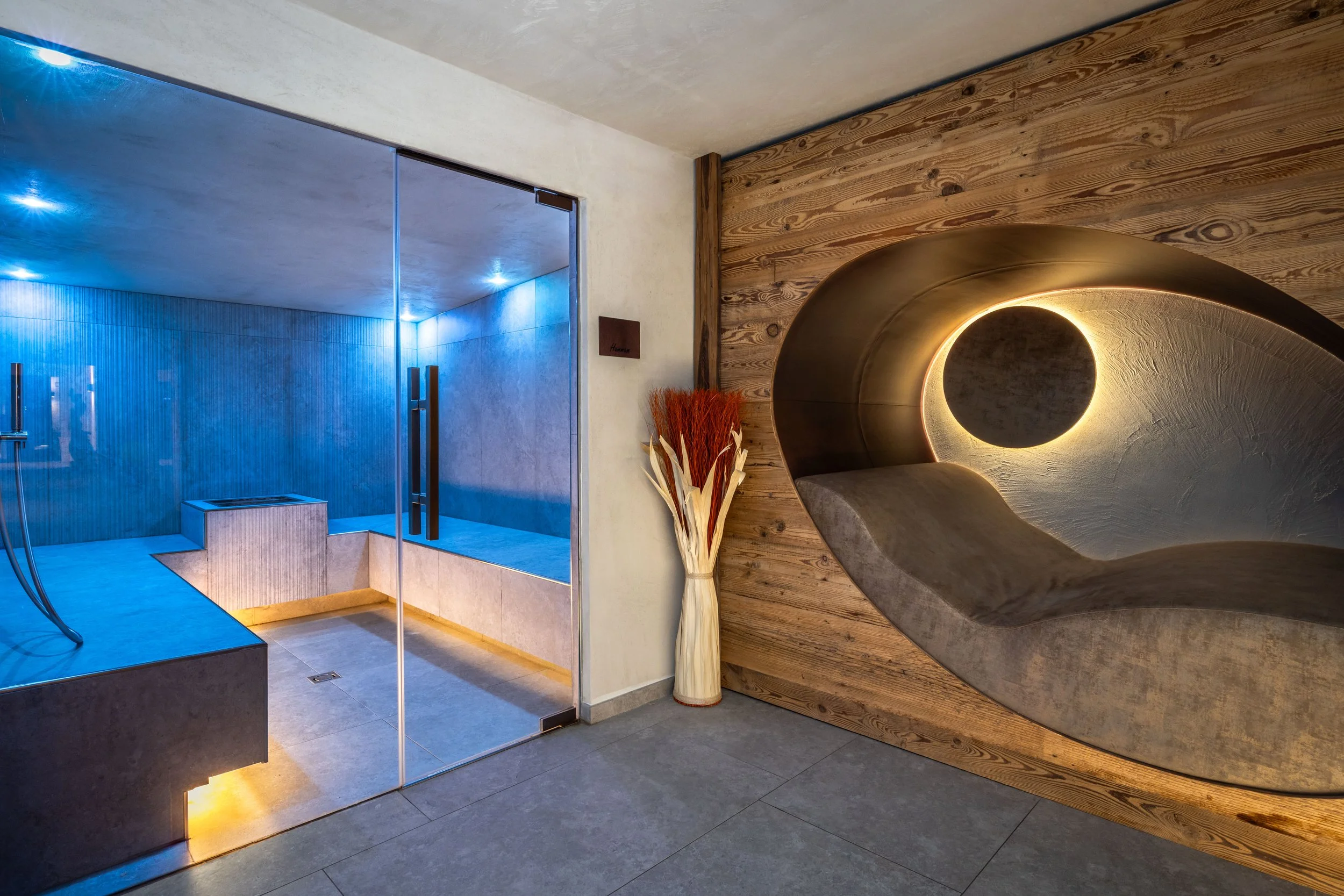 Interno di una spa con sauna in legno e un'area di doccia con pareti di vetro blu.