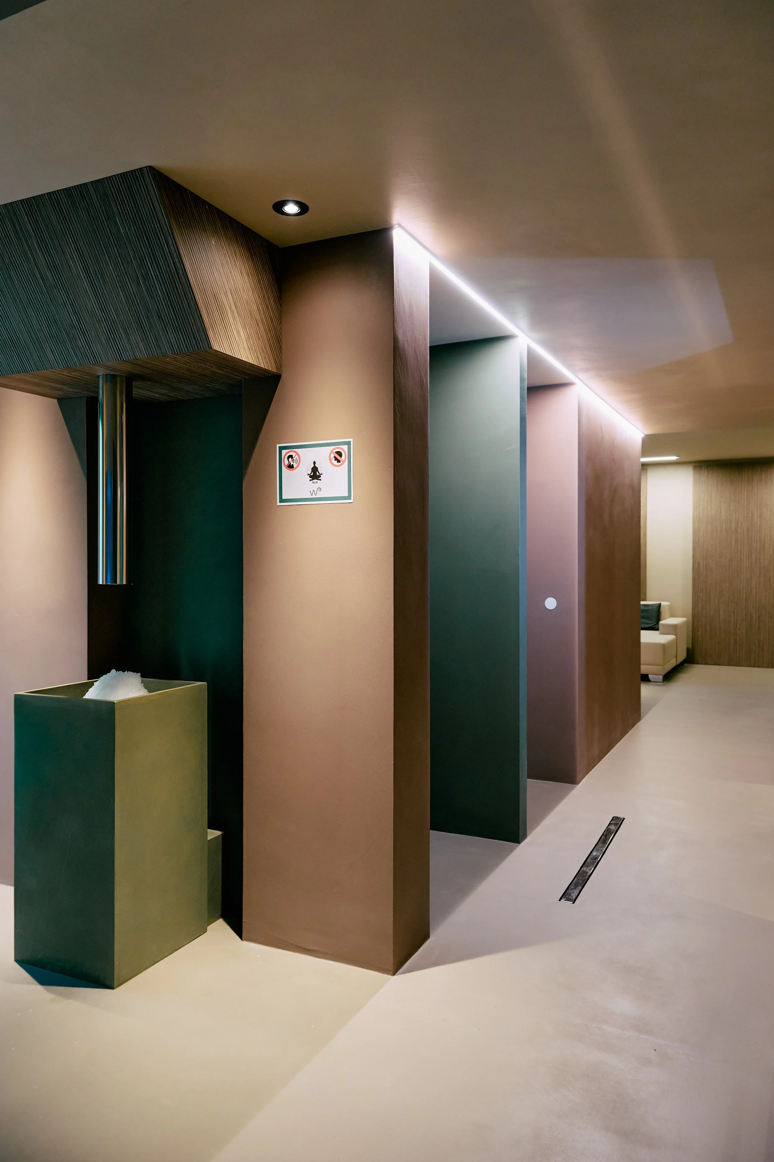 Interno di un edificio con pareti colorate, un cartello con simboli di divieto e un'area relax con divani, illuminazione moderna.