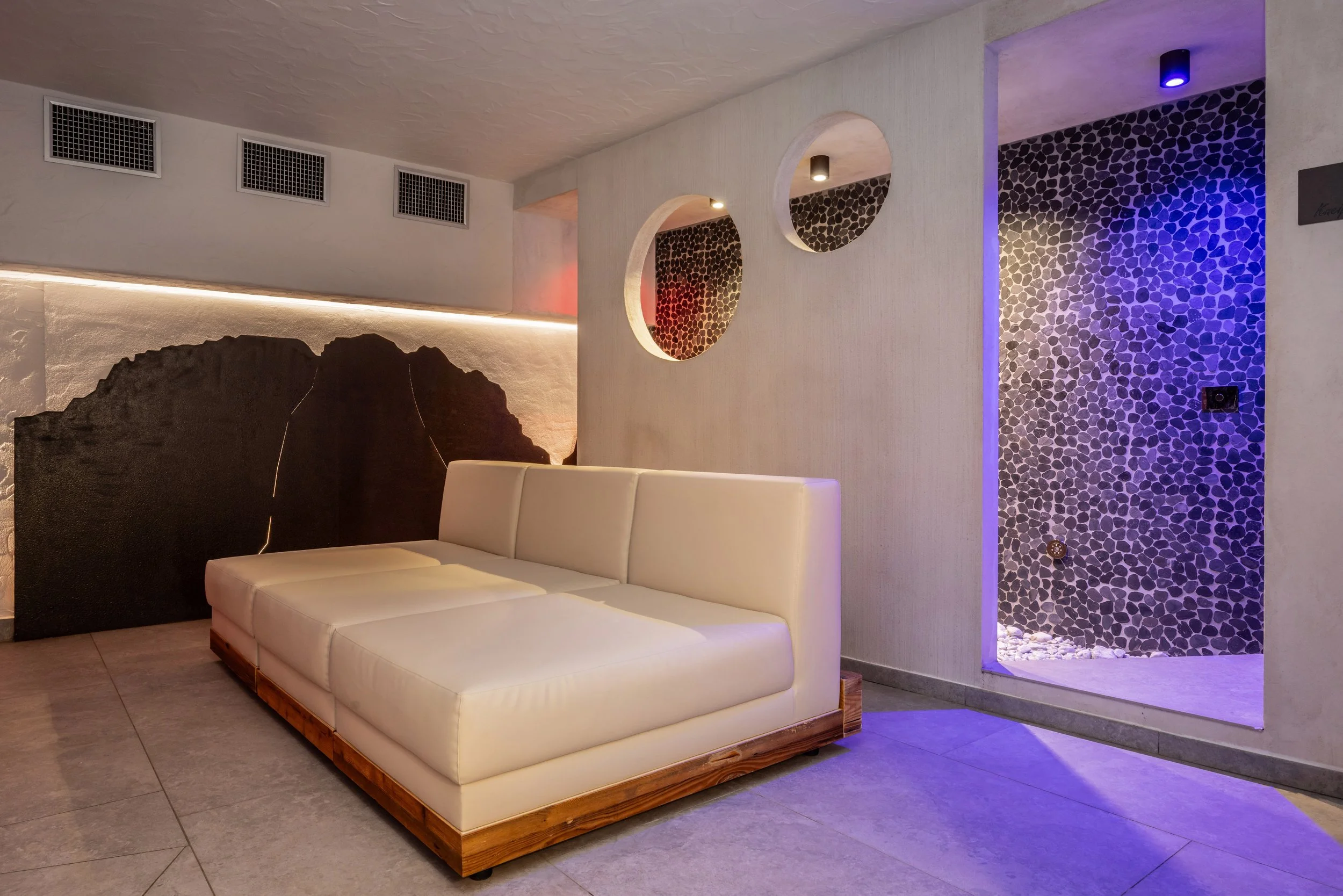 Soggiorno con divano bianco in stile minimalista e pareti decorativi con luci colorate e pareti di pietra