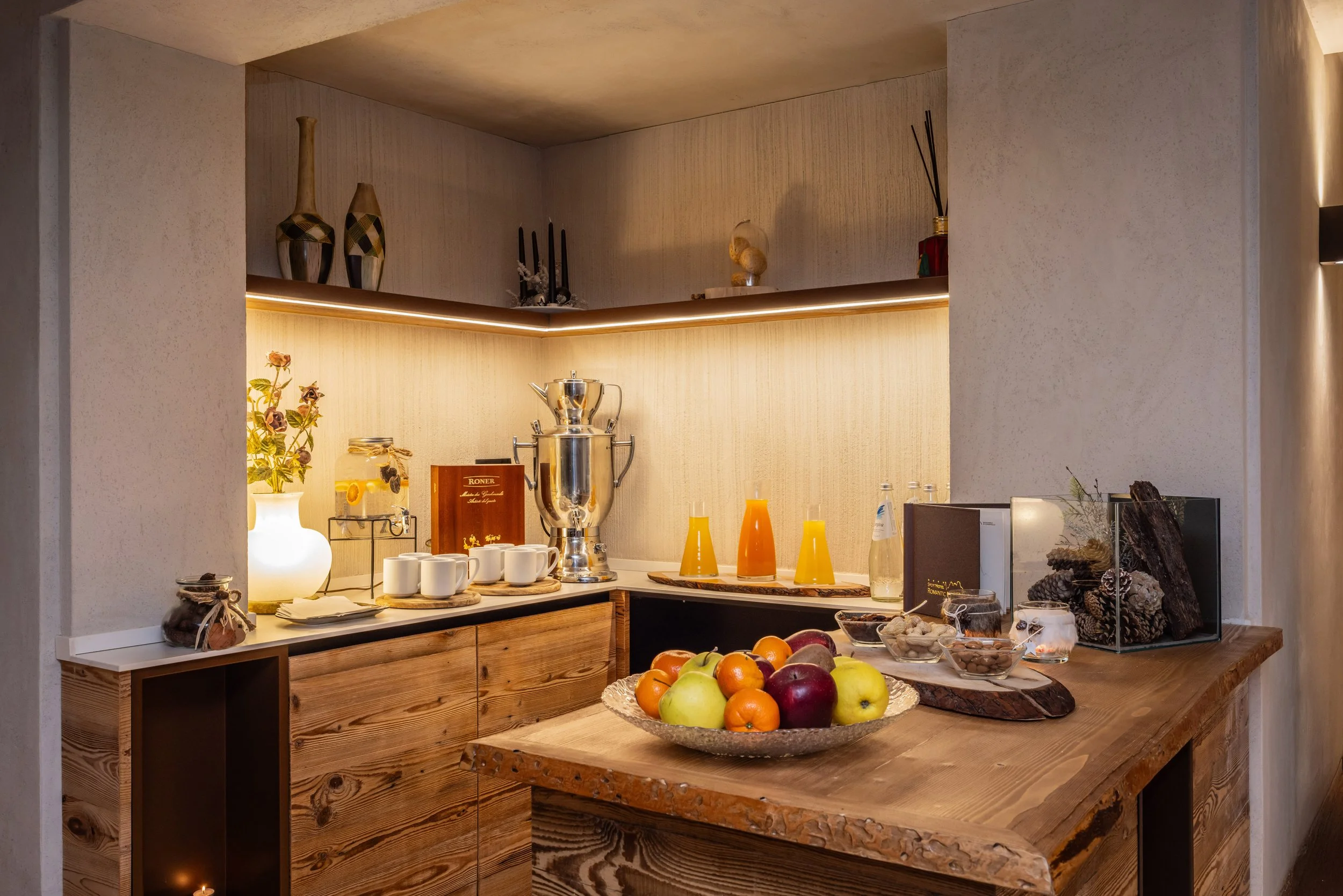 Un bancone con vari fiori e frutta, sullo sfondo una cucina con oggetti decorativi e stoviglie in ceramica.