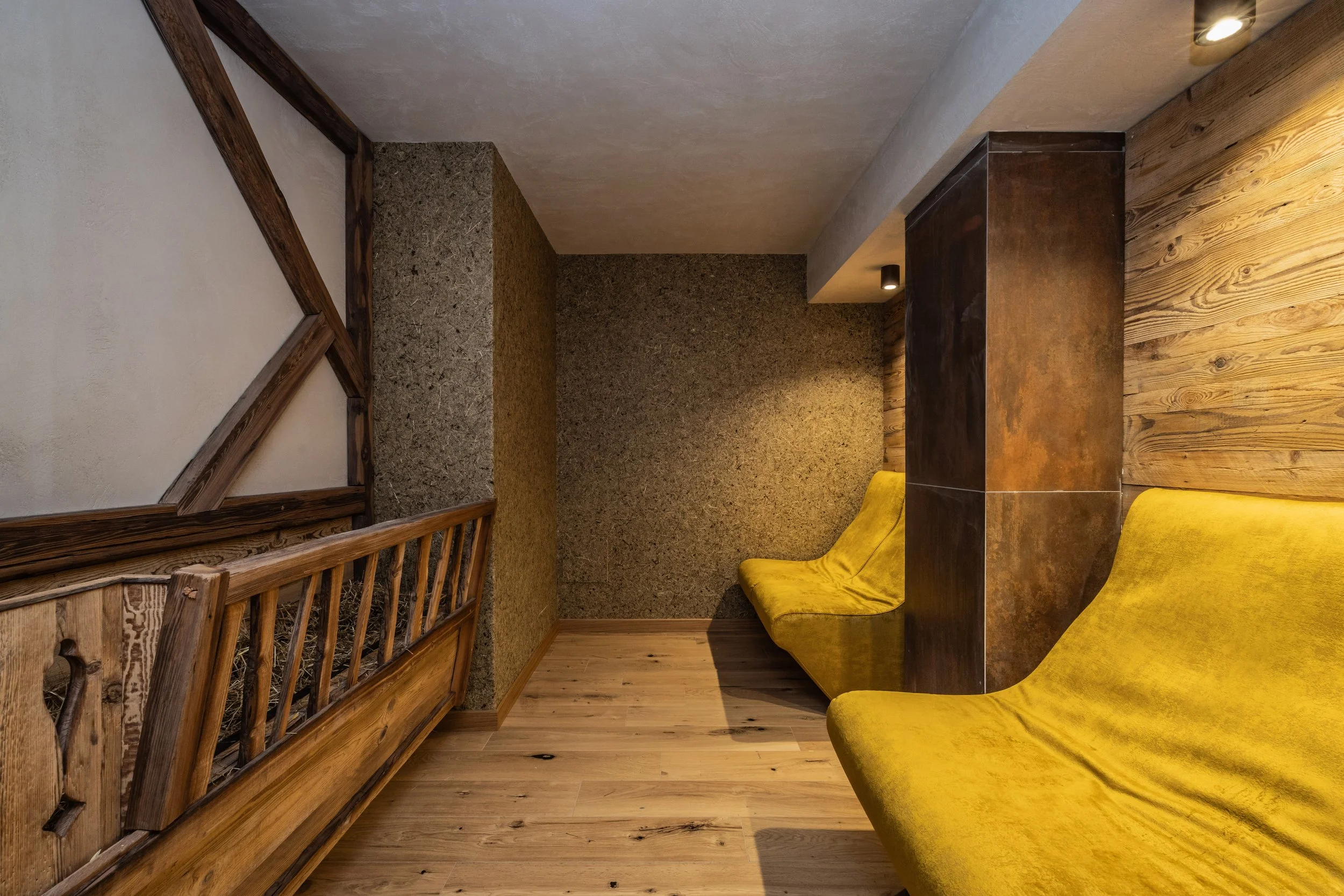 Interno di un locale con pavimenti in legno, sedie gialle, pareti in pietra e legno, e decorazioni di legno sulla parete di sinistra.
