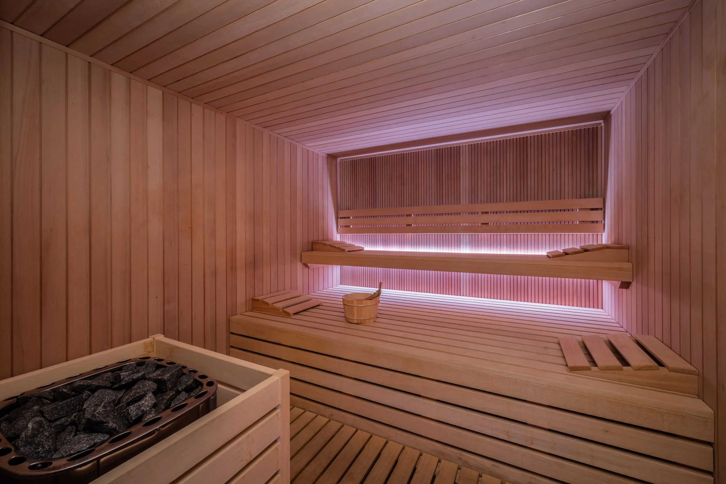 Interno di una sauna in legno con sedili e ciotola di acqua, illuminazione soffusa
