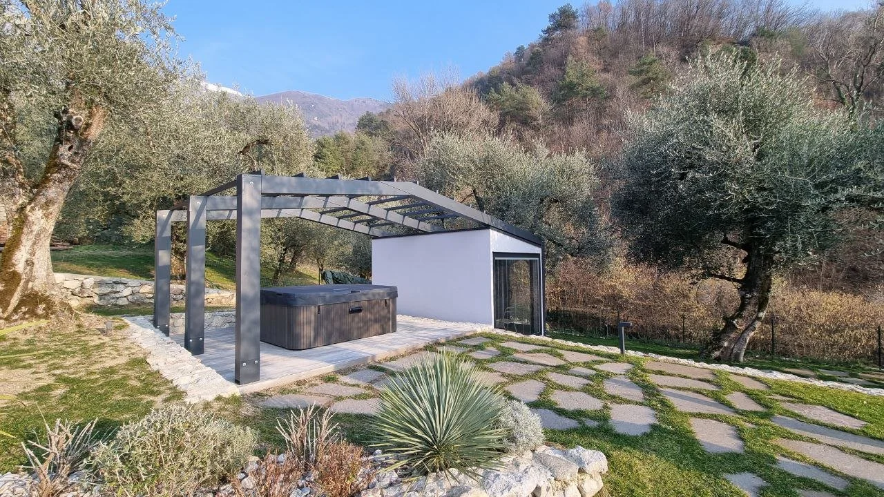 Zona relax all'aperto con sauna, jacuzzi e area pavimentata con pietre, circondata da alberi e natura montana.