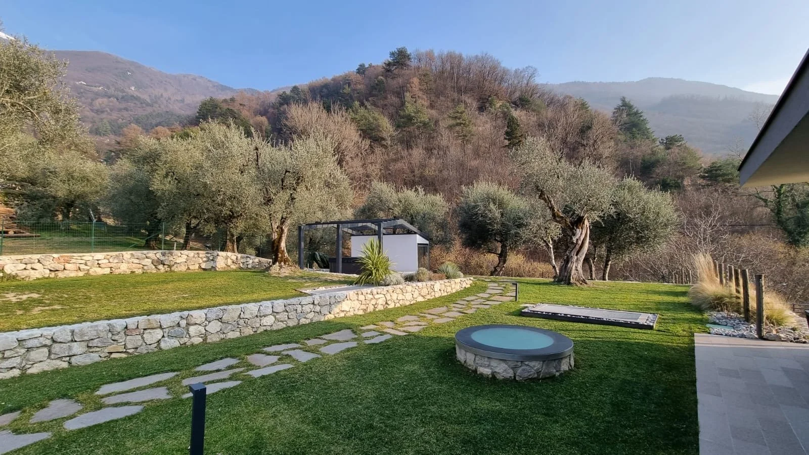 Giardino con ciottoli, fontana rotonda, panchina, alberi e montagne sullo sfondo
