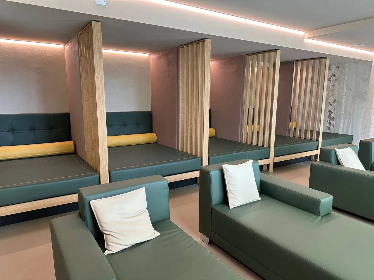 Soggiorno con divani verdi e lettini in stile capsule con pannelli di legno divisori, illuminazione a LED soffusa.