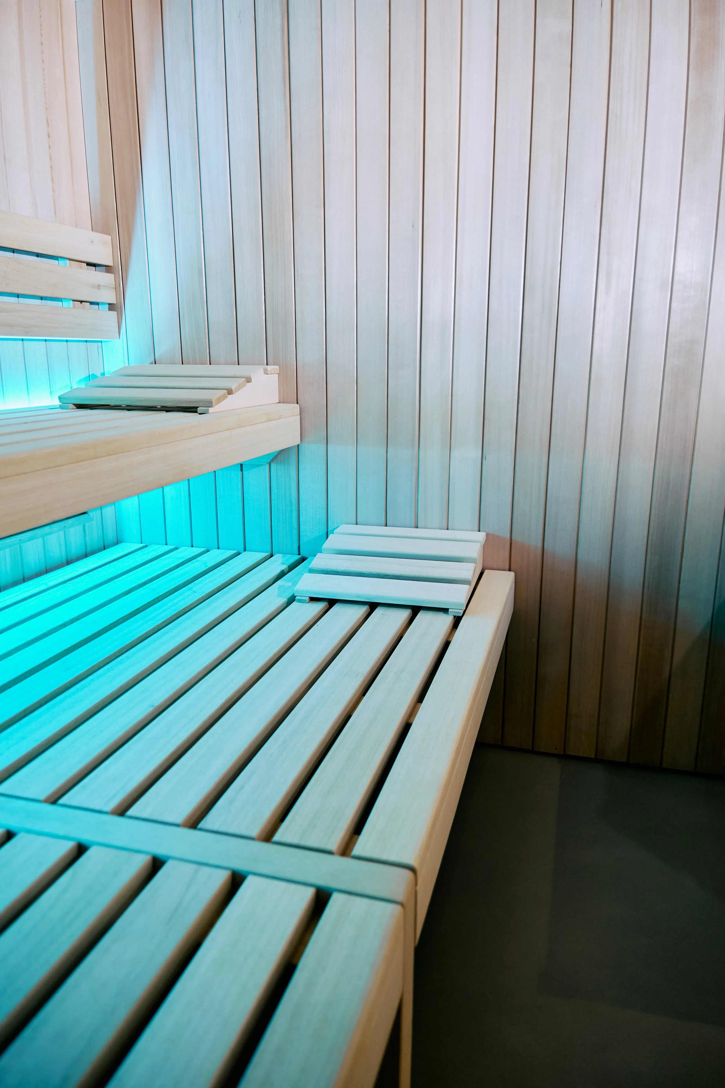 Interno di una sauna con sedili di legno e pannelli in legno alle pareti, illuminata da luci soffuse di colore blu.
