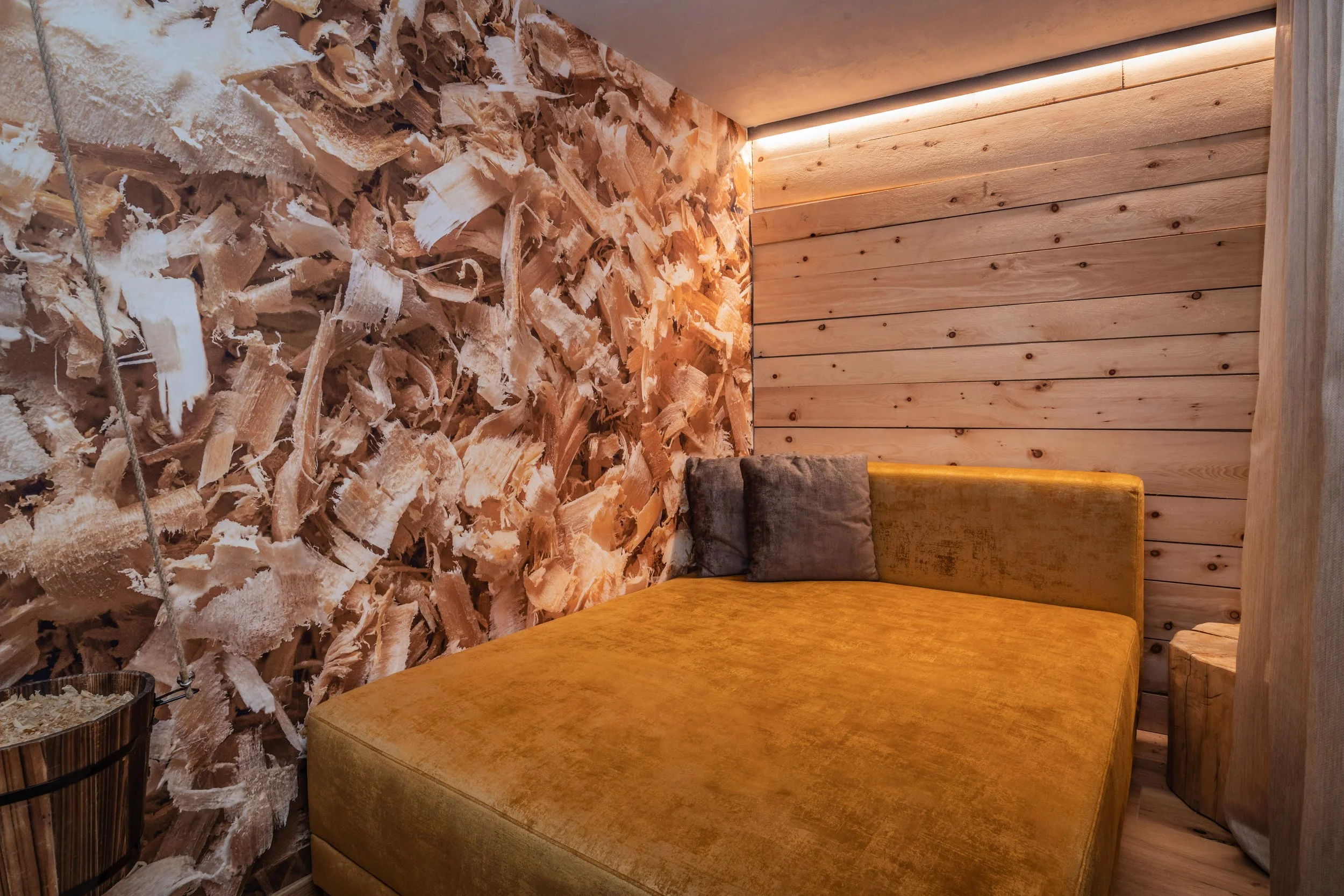 Interno di una stanza con pareti di legno, un divano color senape, e una parete decorativa di trucioli di legno