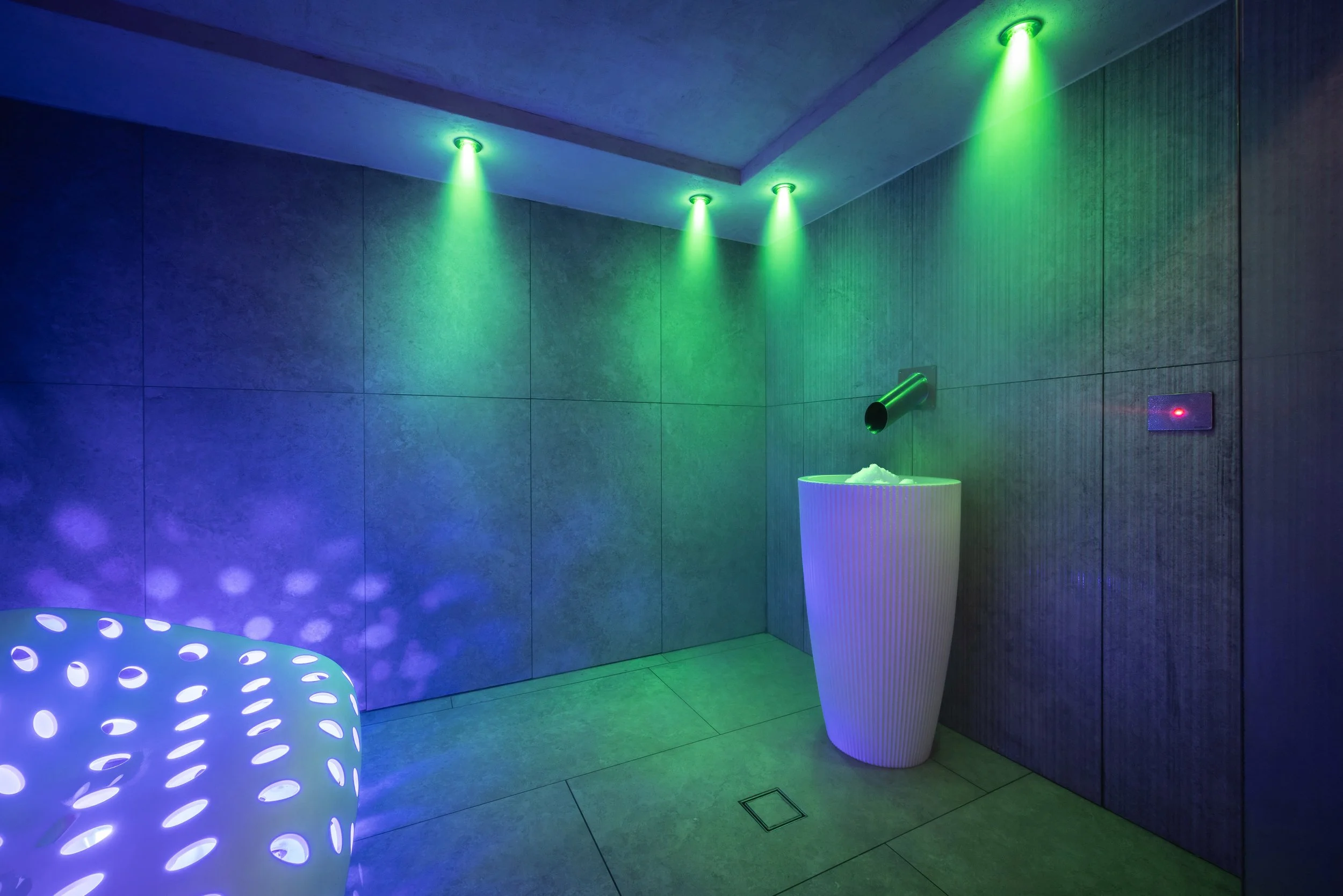 Stanza moderna con luci soffuse verdi e blu, vasca da bagno rotonda con luce viola, grande vaso bianco, pareti di legno e pavimento di piastrelle