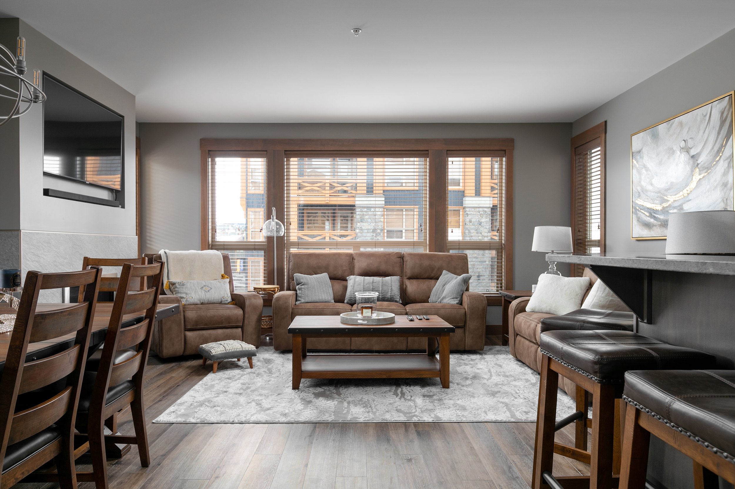 Big White Resort condo's living room with large windows, leather sofas, and wooden furniture.
