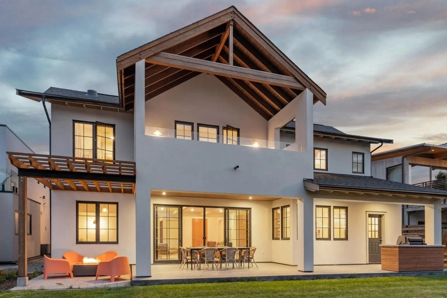Modern two-story house with large windows, a balcony, and an outdoor patio area at sunset.
