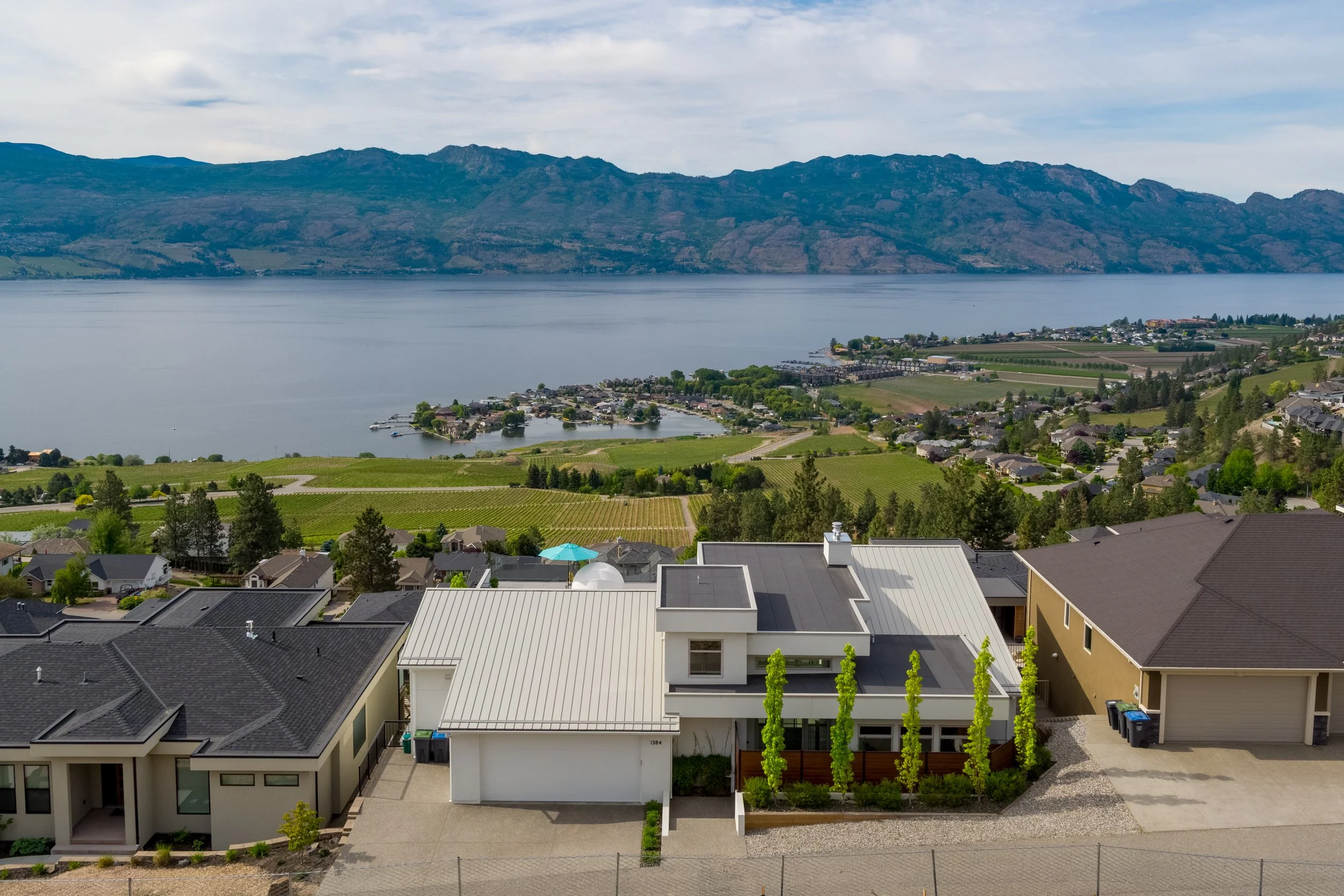 Pinot Noir Drive residential home with modern architecture, mountains, and a lake in the background under a cloudy sky.