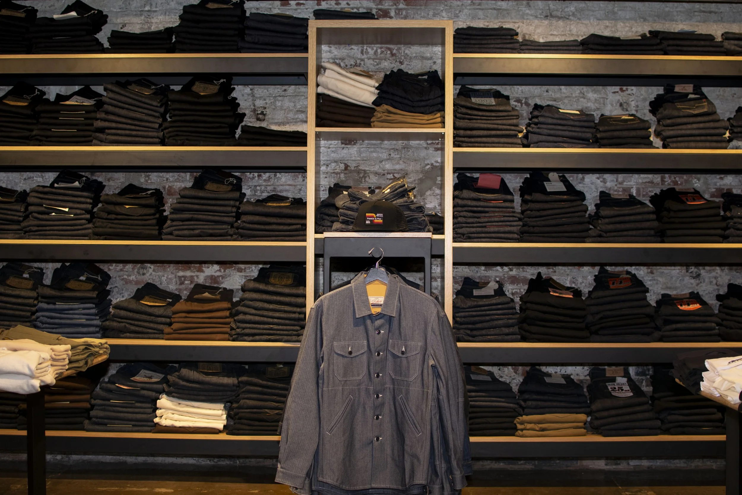 Overall view of inside Franklin and Poe clothing store with steel and wood displays holding folded mens shirts, boots and denim. 