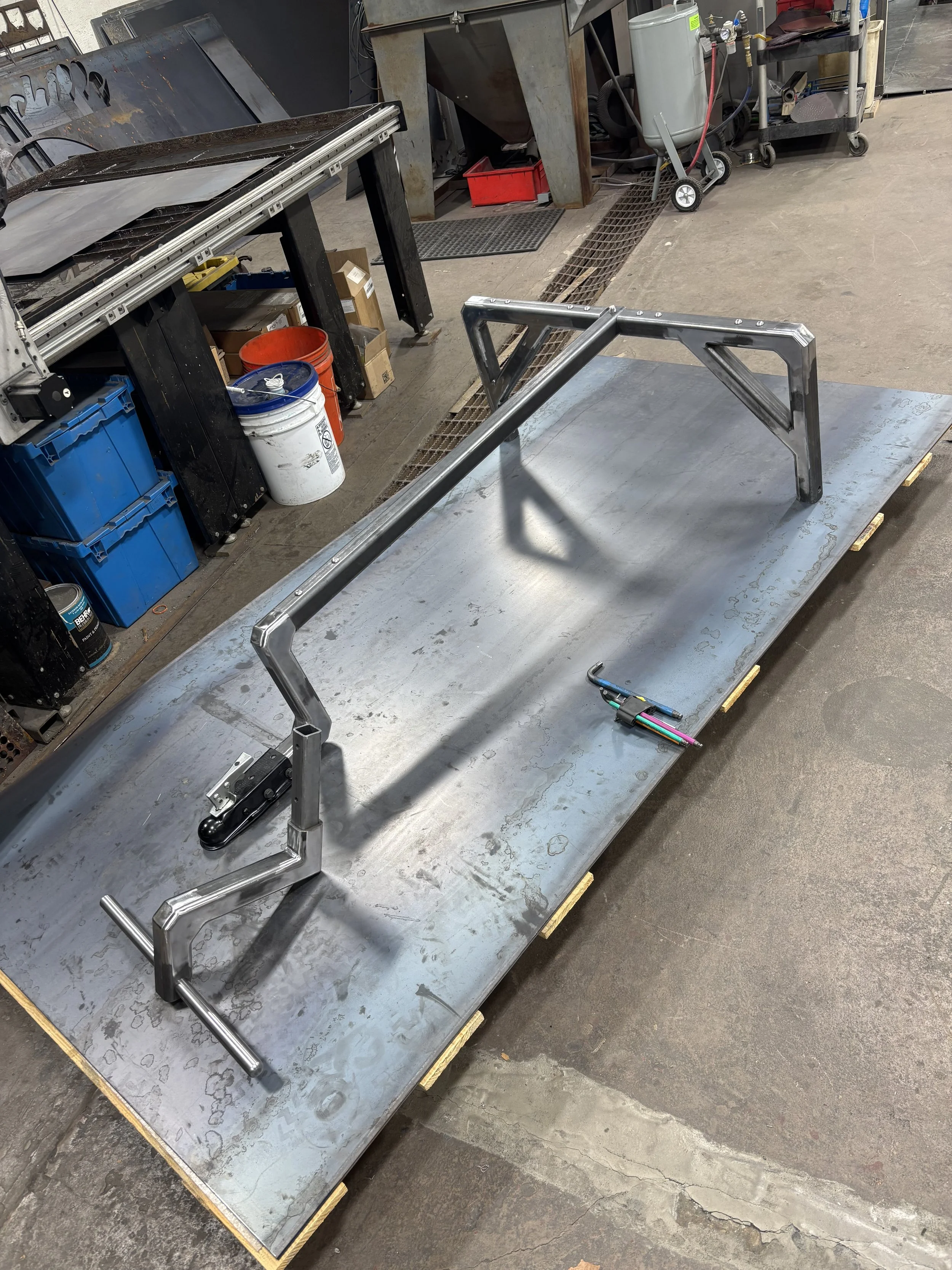 Metal workbench with metal frame being assembled, workshop with various tools, parts, and containers in background.