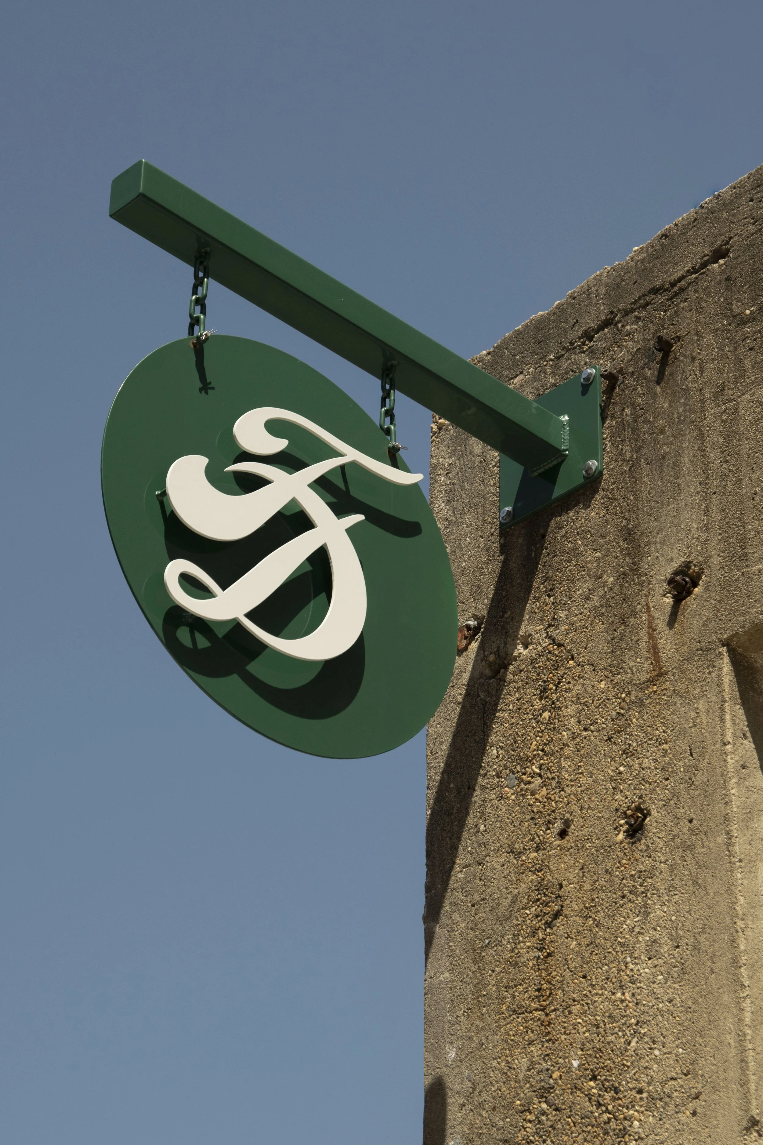 Close-up of a green store sign mounted on a rusted concrete wall, with a plain blue sky in the background.