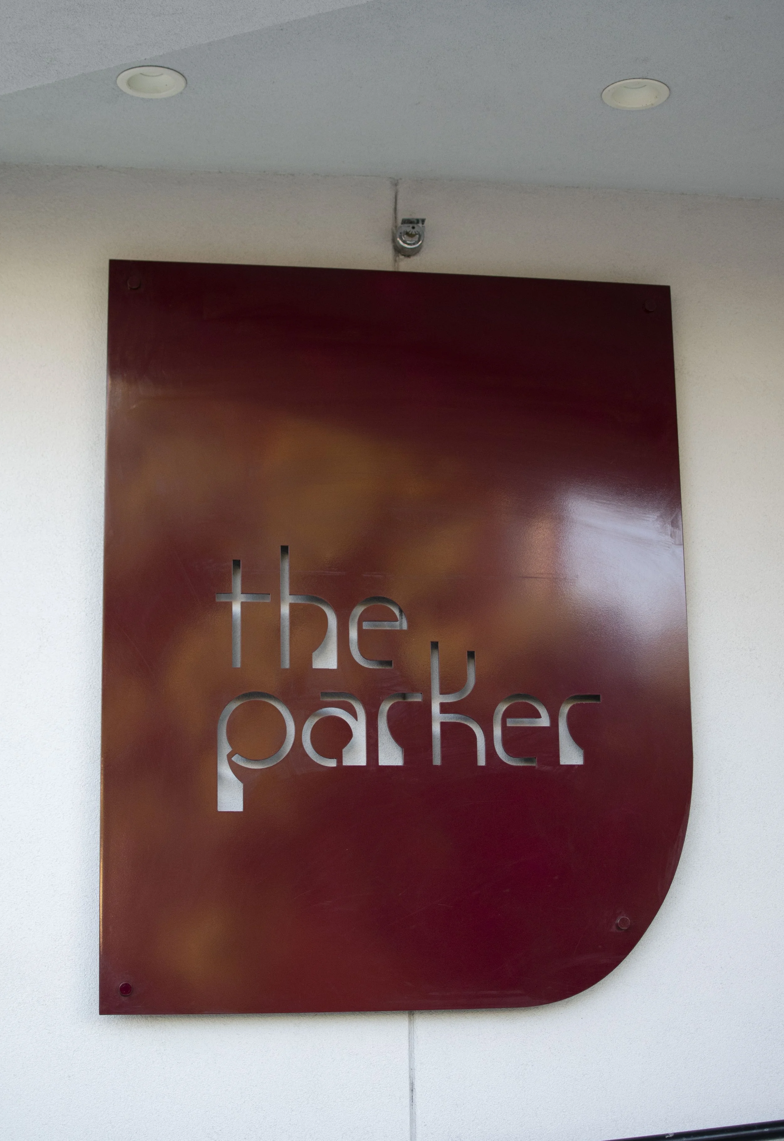 A burgundy sign with ' the parker' cut out from it.  The sign is mounted on a white wall.