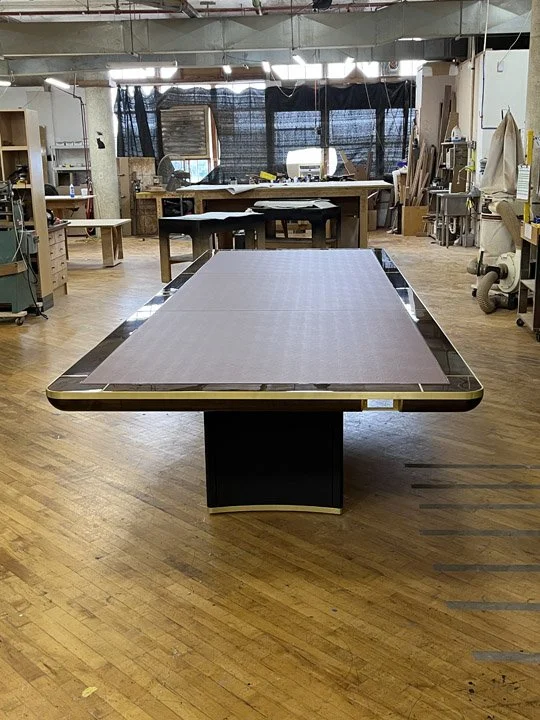 Empty drafting table in an artist's or designer's studio with various art supplies and equipment in the background.