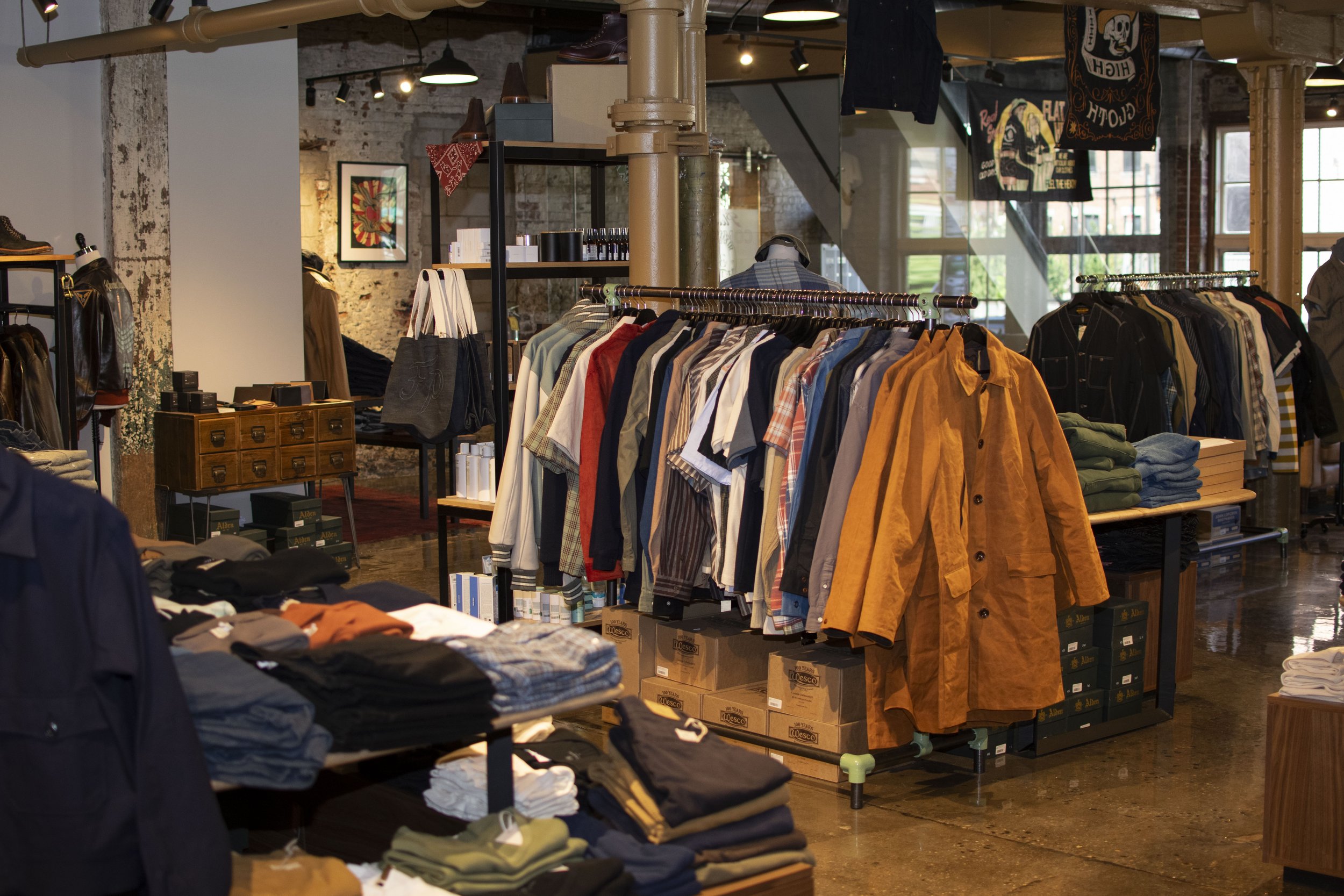 Overall view of inside Franklin and Poe clothing store with steel and wood displays holding folded mens shirts, boots and denim. 