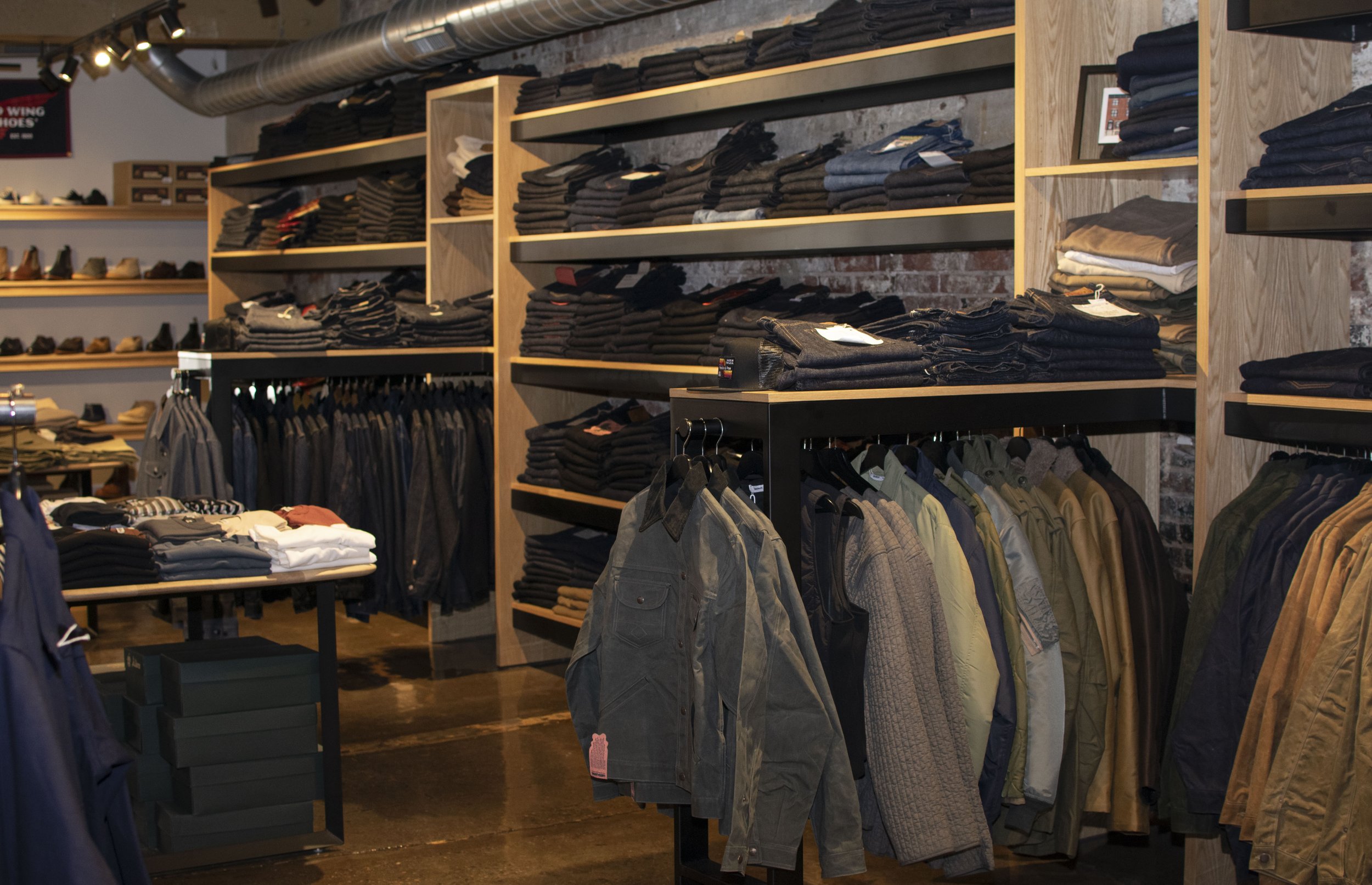 Overall view of inside Franklin and Poe clothing store with steel and wood displays holding folded mens shirts, boots and denim. 