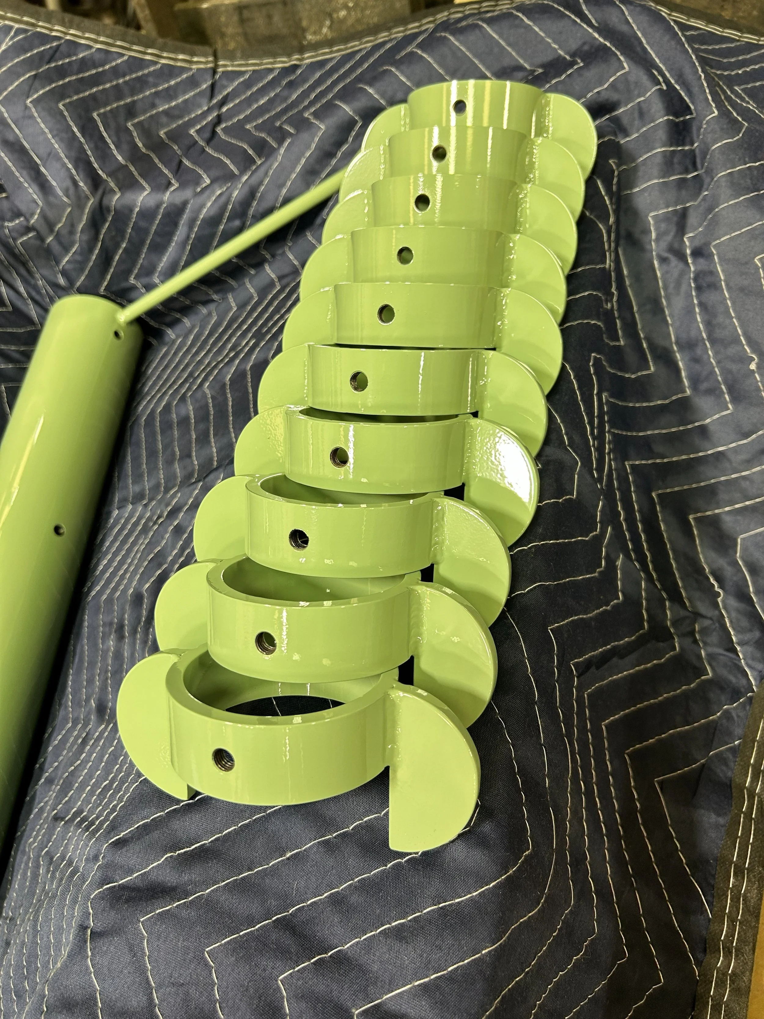 A green spacer clip with multiple curved pieces stacked together, holes in each piece, resting on a blue fabric.