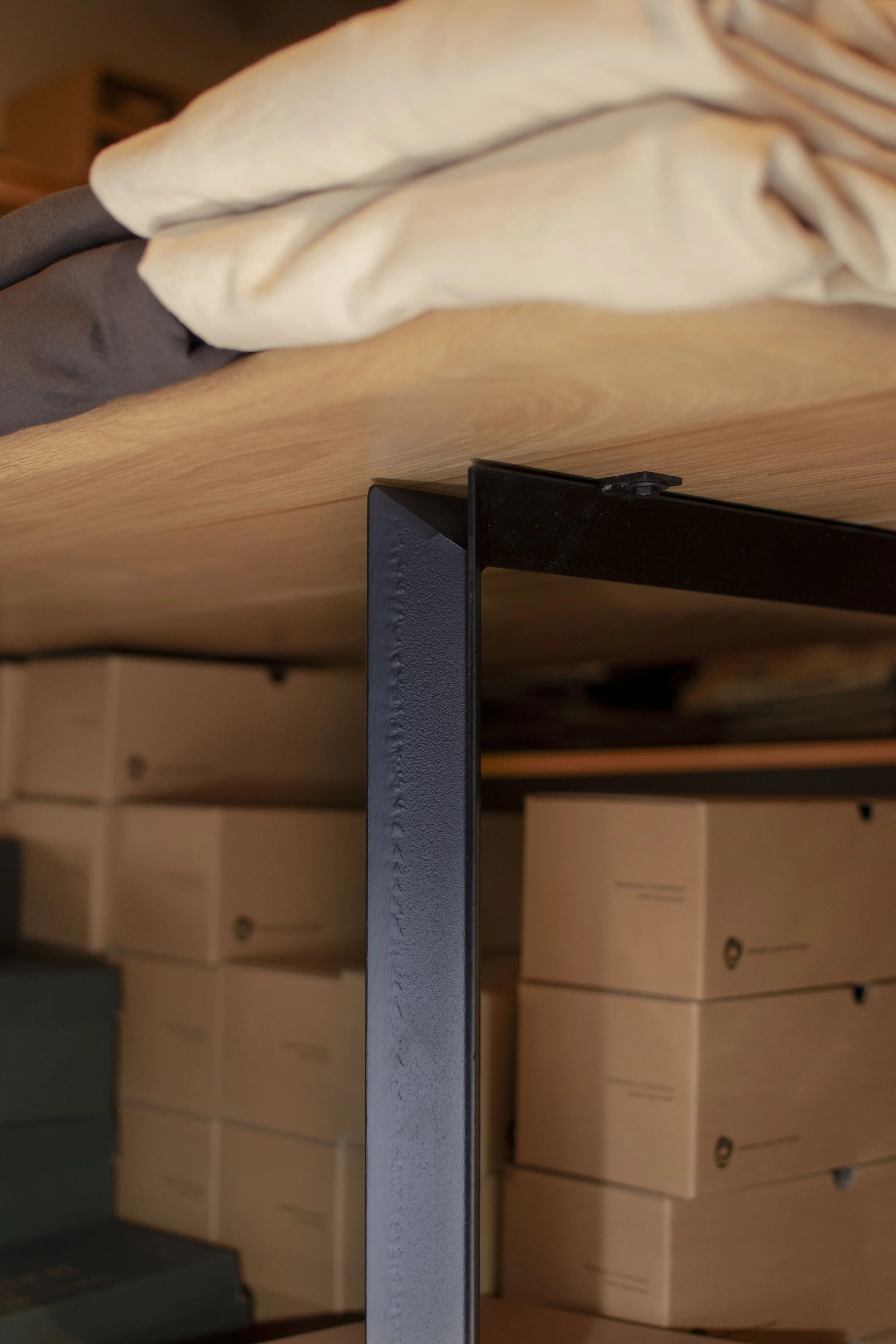 Detail of angle iron intersecting with wood tops on a display table holding shirts