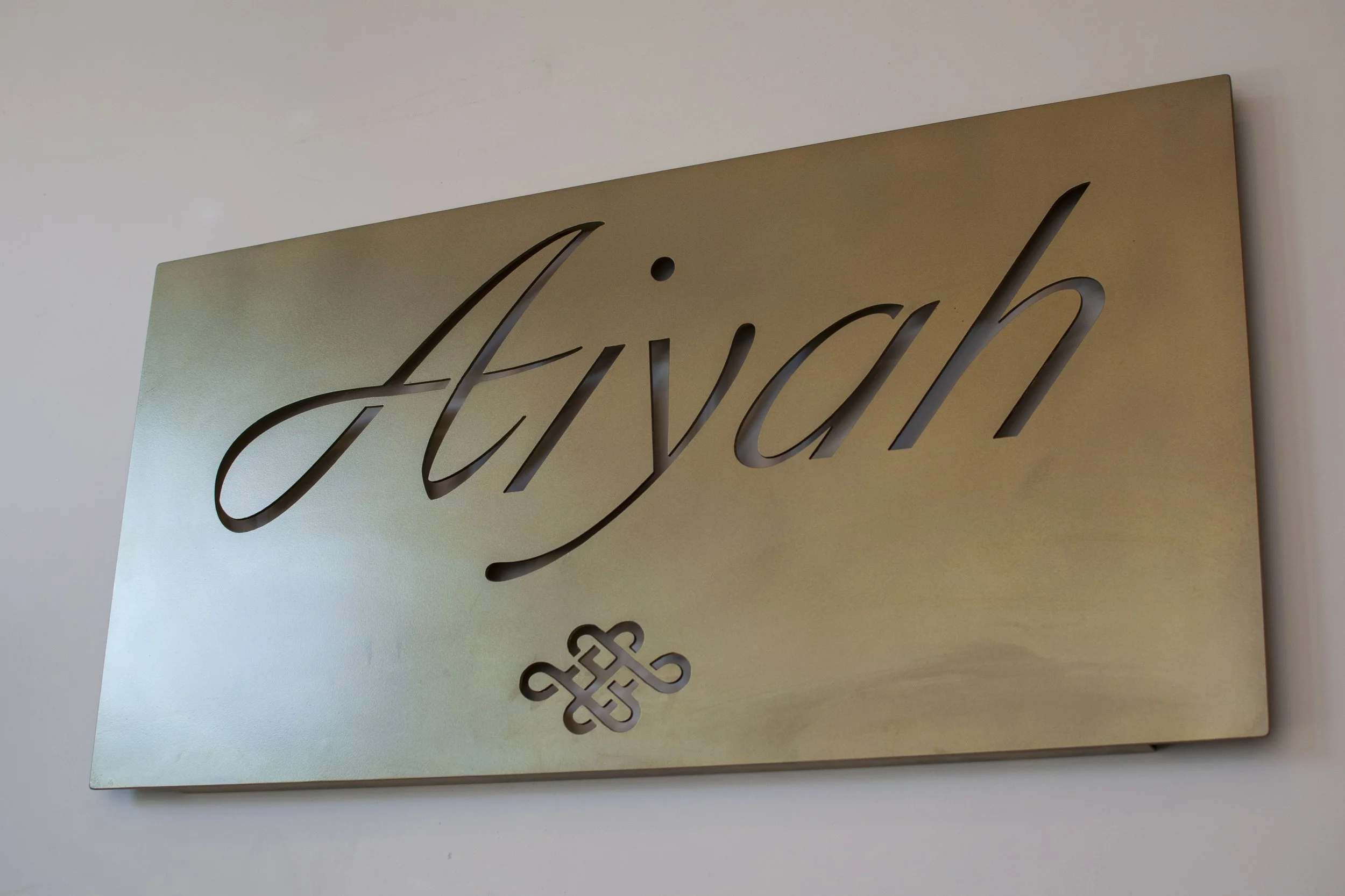 A gold-colored sign with the word 'Aiyah' cut out in cursive script.