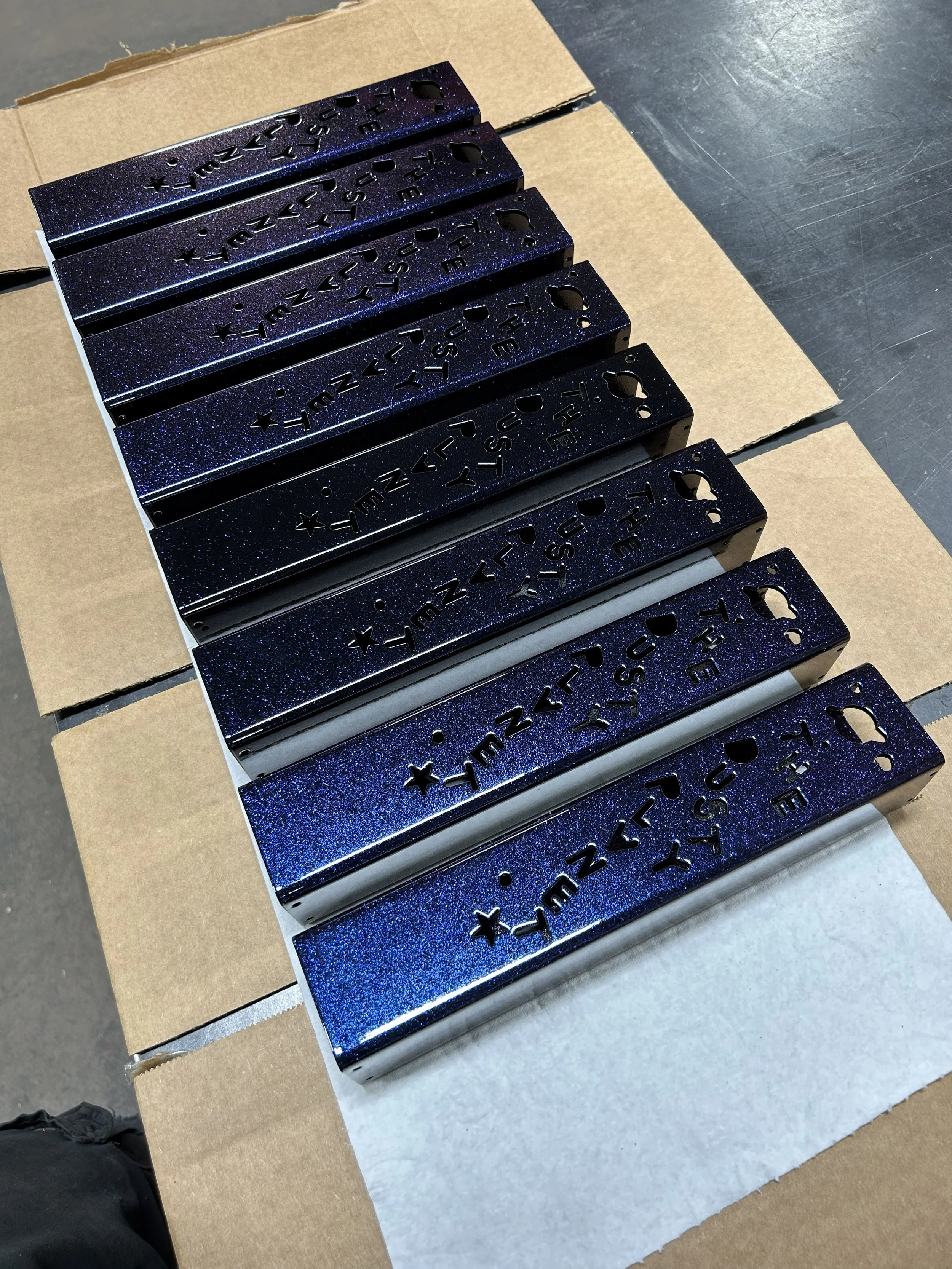 Metal objects with star and text cutouts, finished in a black powder coat with purple and blue glitter throughout.