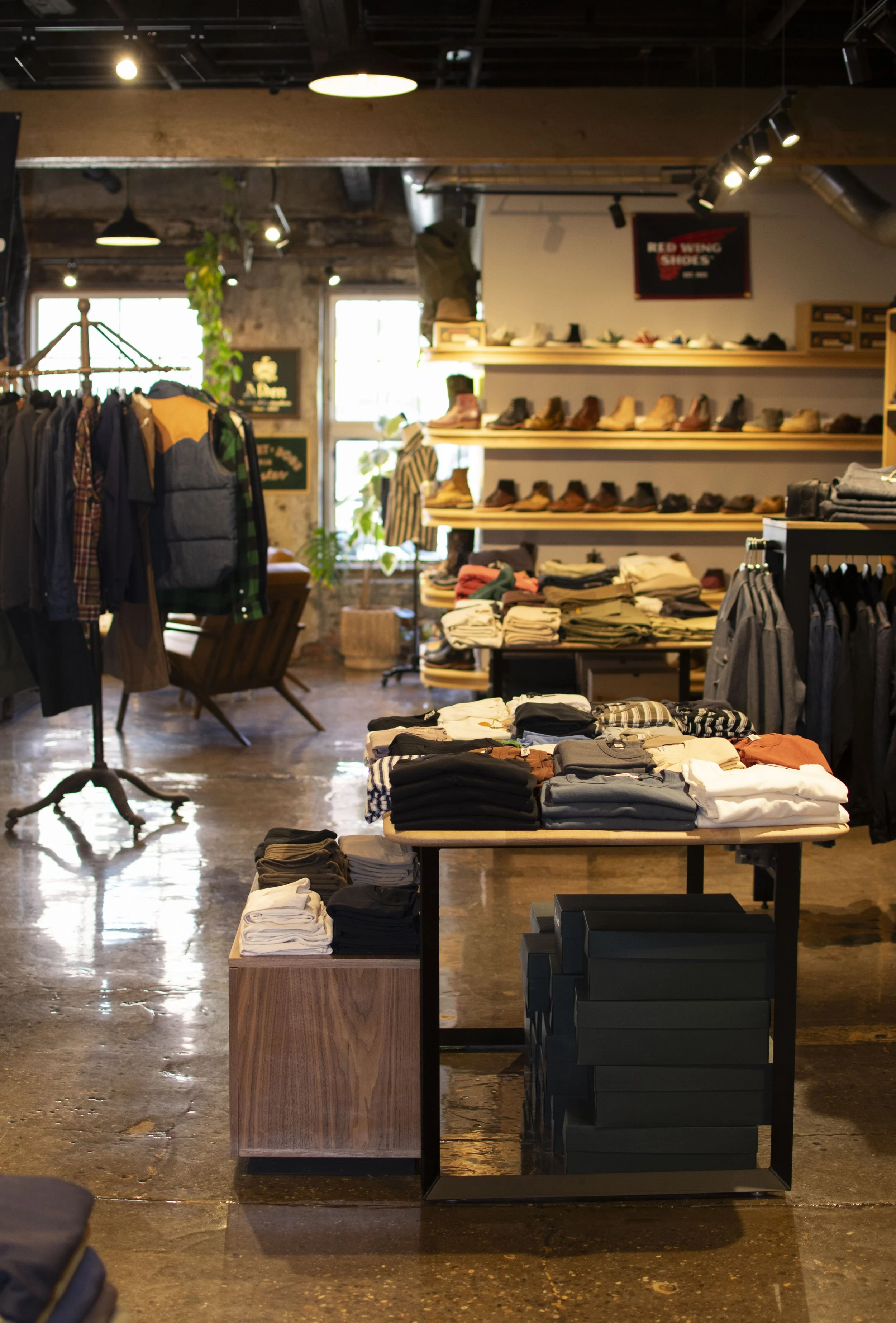 Overall view of inside Franklin and Poe clothing store with steel and wood displays holding folded mens shirts, boots and denim. 